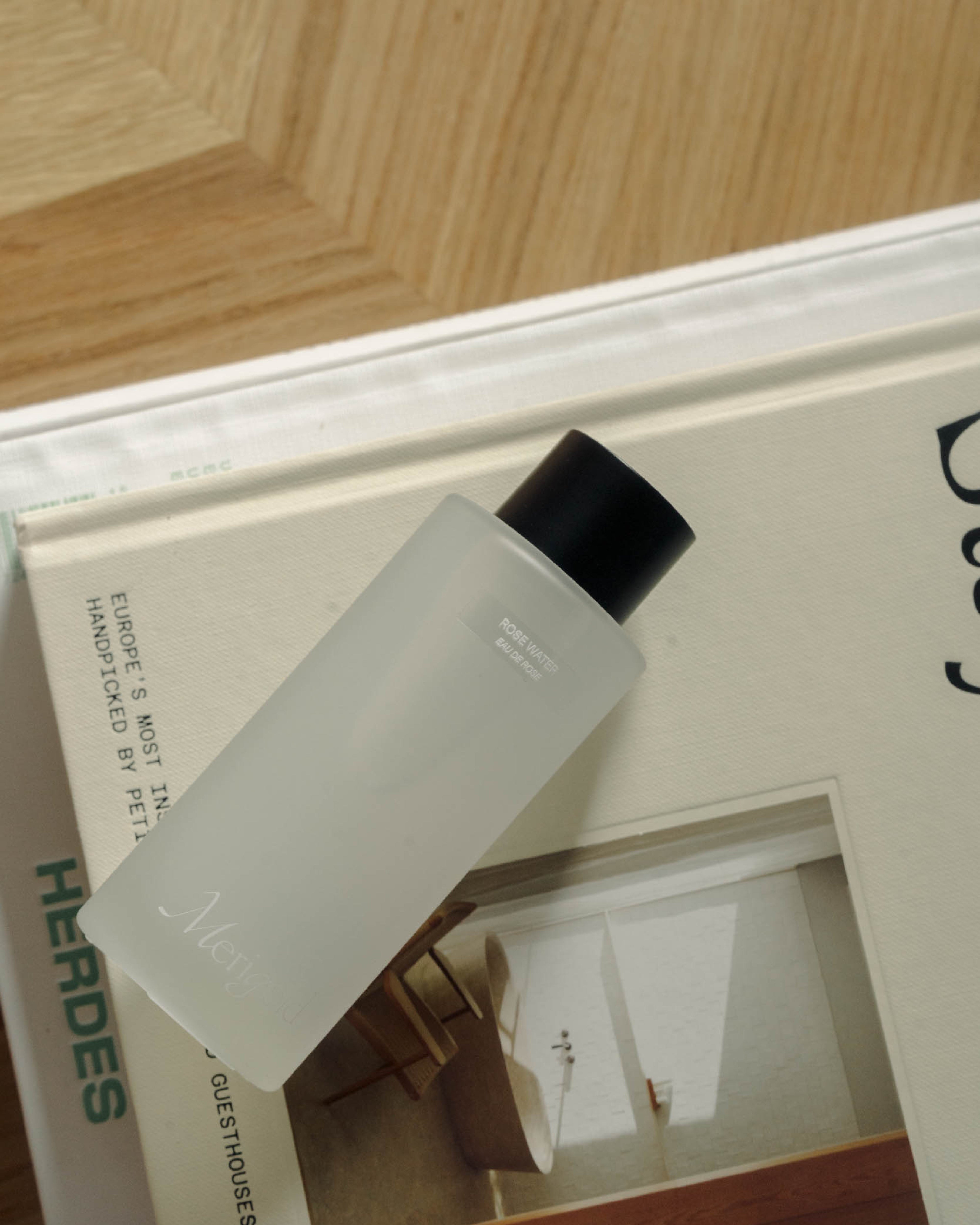 Merigold Rose Water bottle styled on neutral books and wood surface – hydrating, soothing floral toner for dry and sensitive skin. Clean, plant-based skincare.