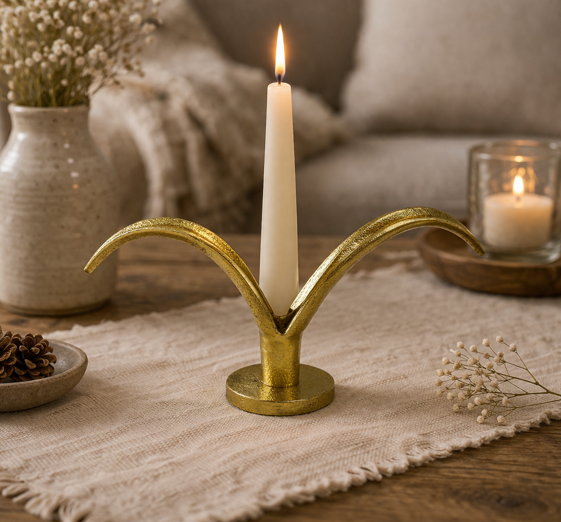 Gold candle holder with a lit candle on a table with decorative elements.
