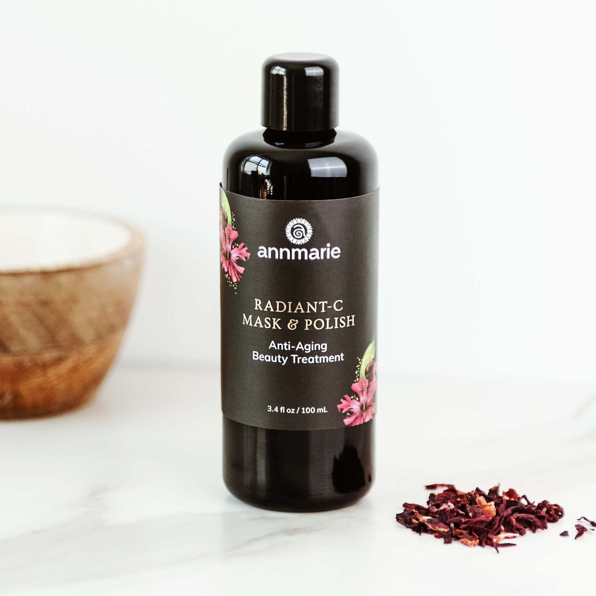 Radiant-C Mask & Polish anti-aging beauty treatment bottle displayed on a clean surface with dried botanical ingredients nearby.