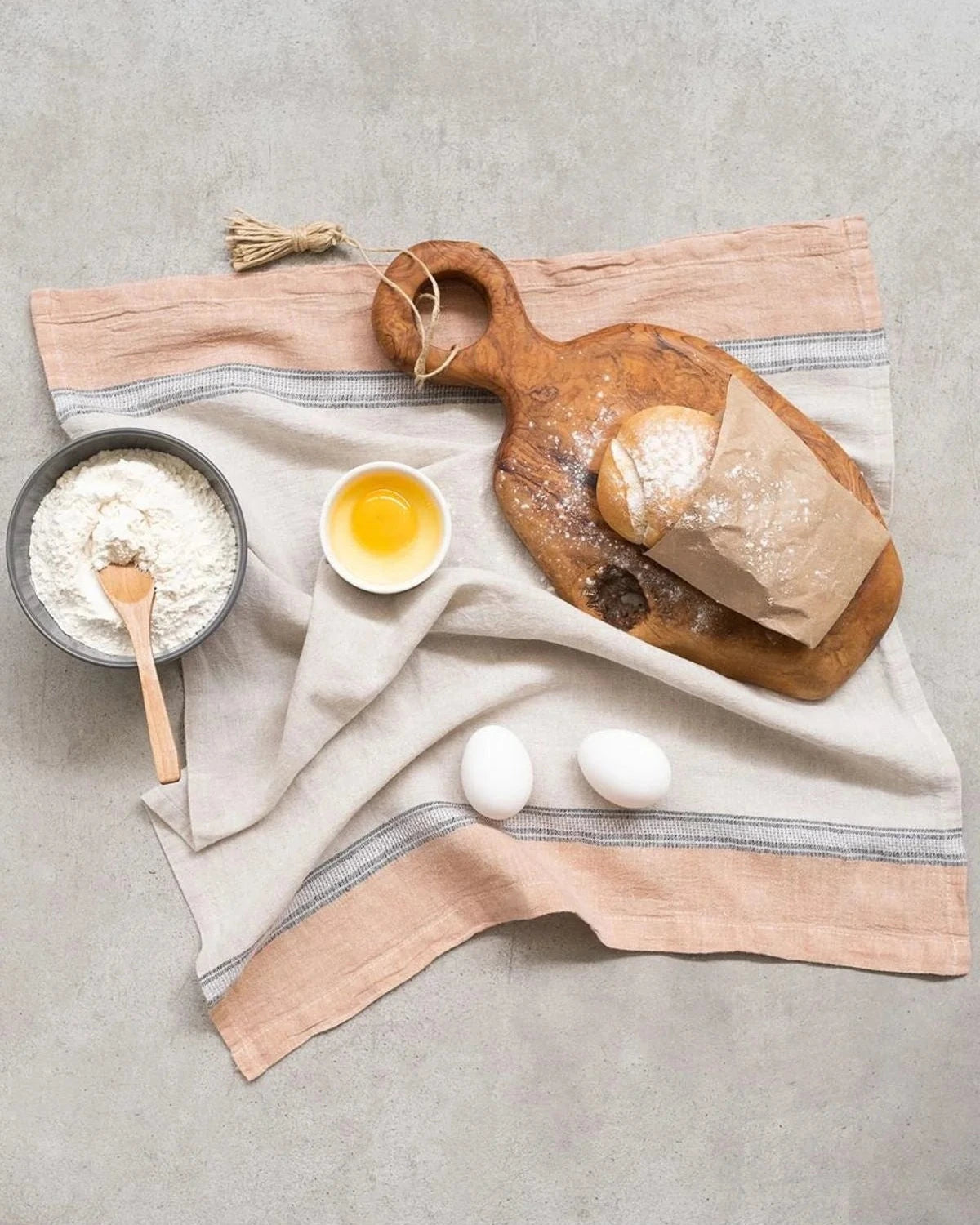 Wooden cutting board with bread, eggs, and flour on a light gray surface
