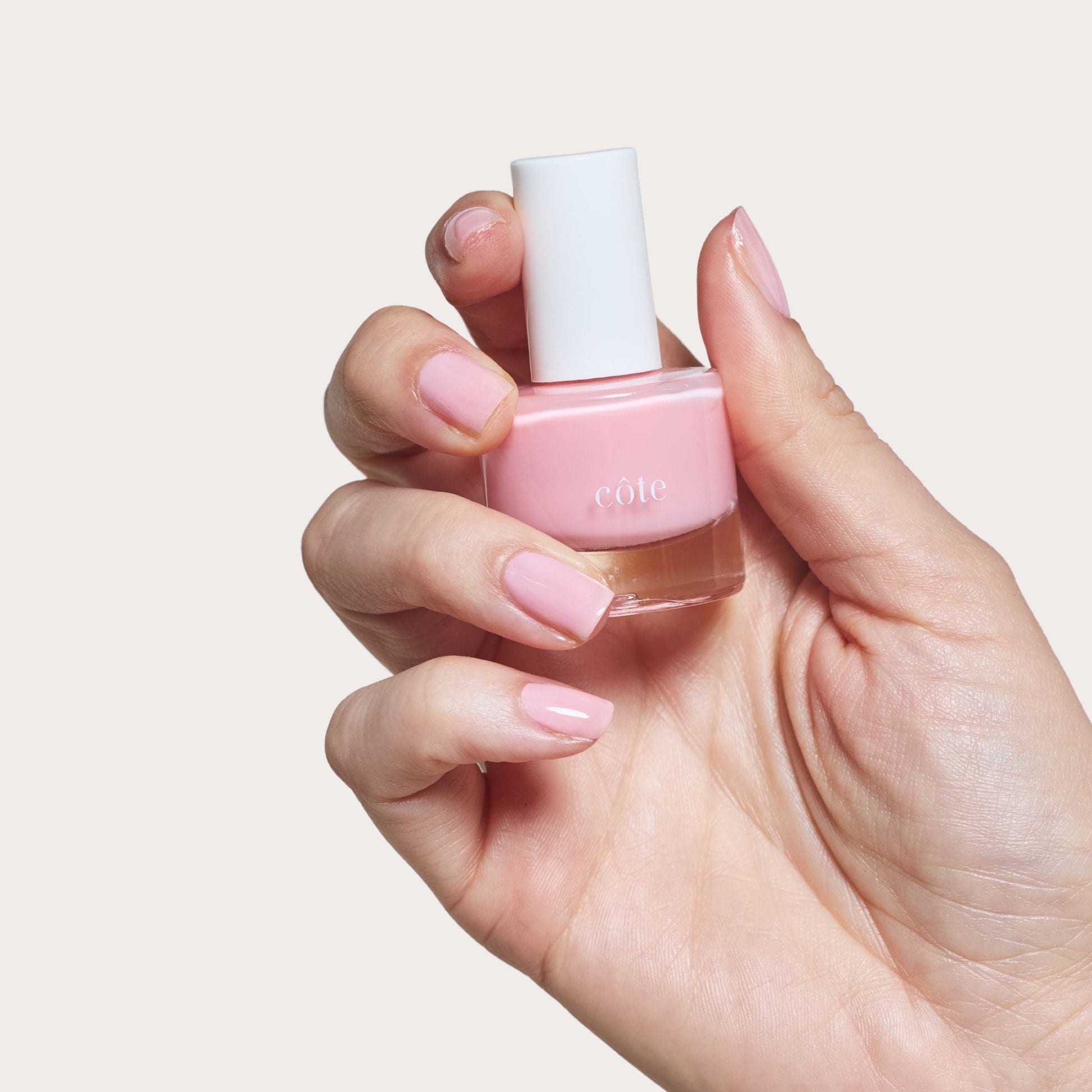 Hand holding Côte Beauty Pink Clouds Sheer Petal Blush Non-Toxic Nail Polish bottle. 