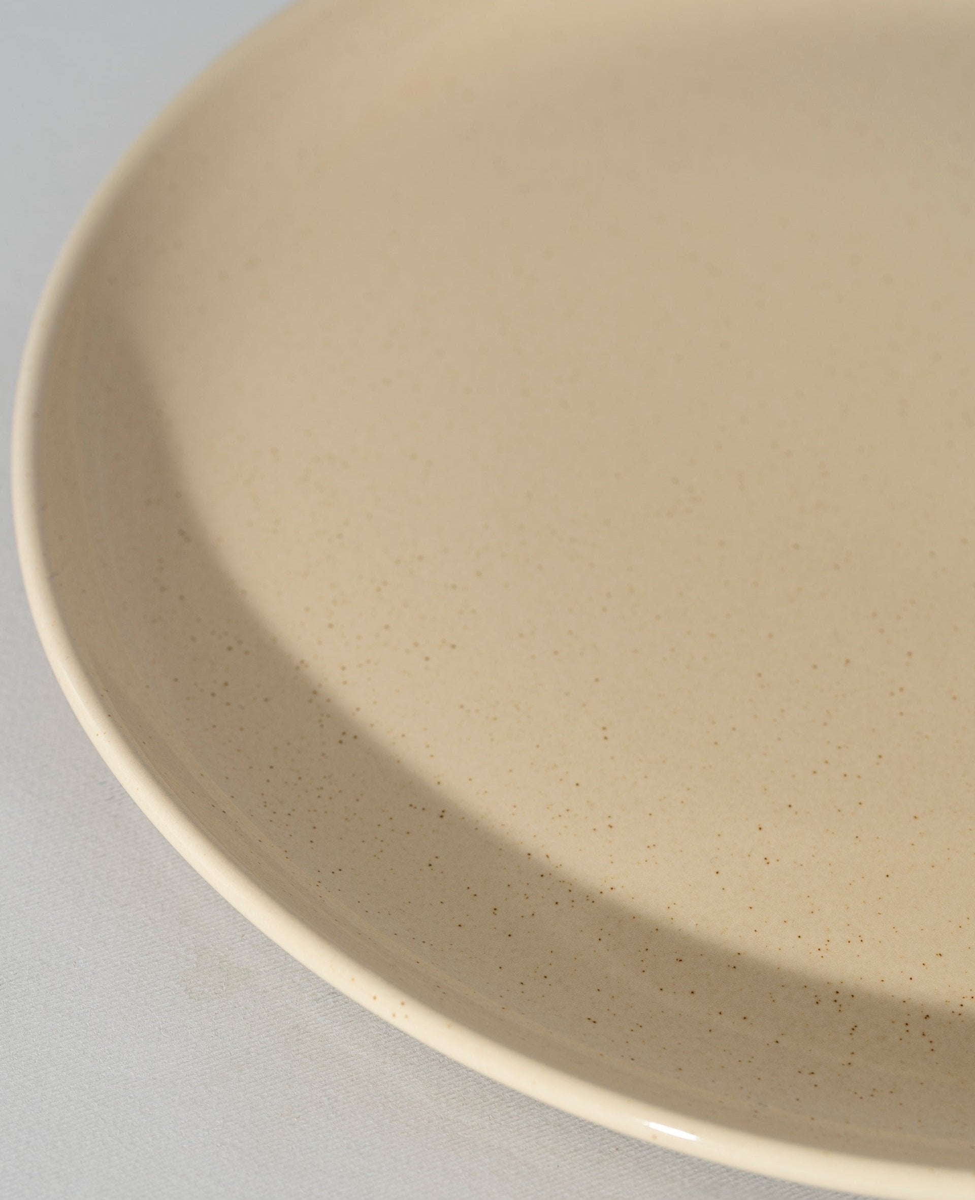 Cream-colored speckled stoneware serving bowl shown from a slight side and middle angle on a white background, emphasizing the smooth, curved interior and soft speckled finish