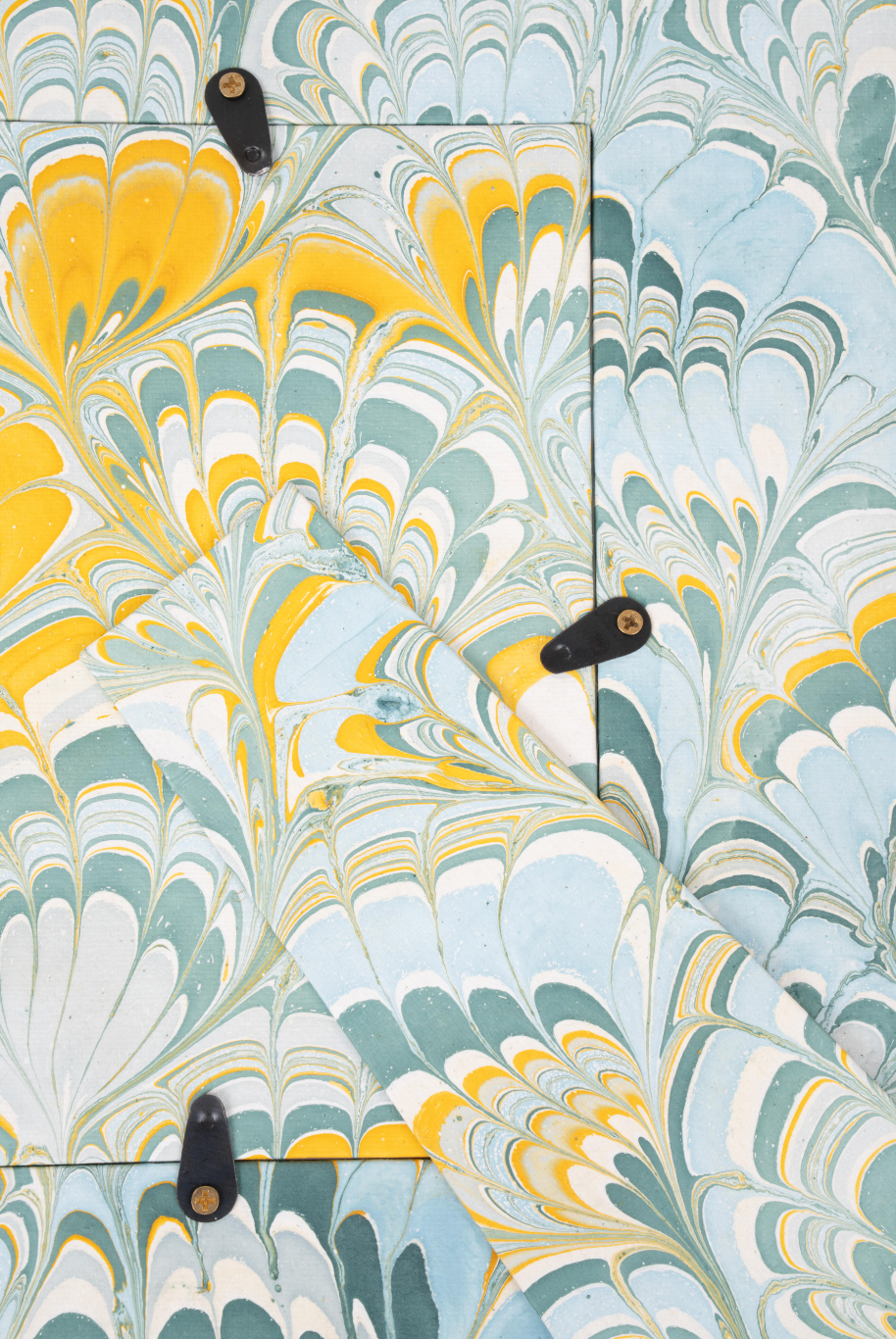 Close-up of hand-marbled blue/yellow paper with black clips,