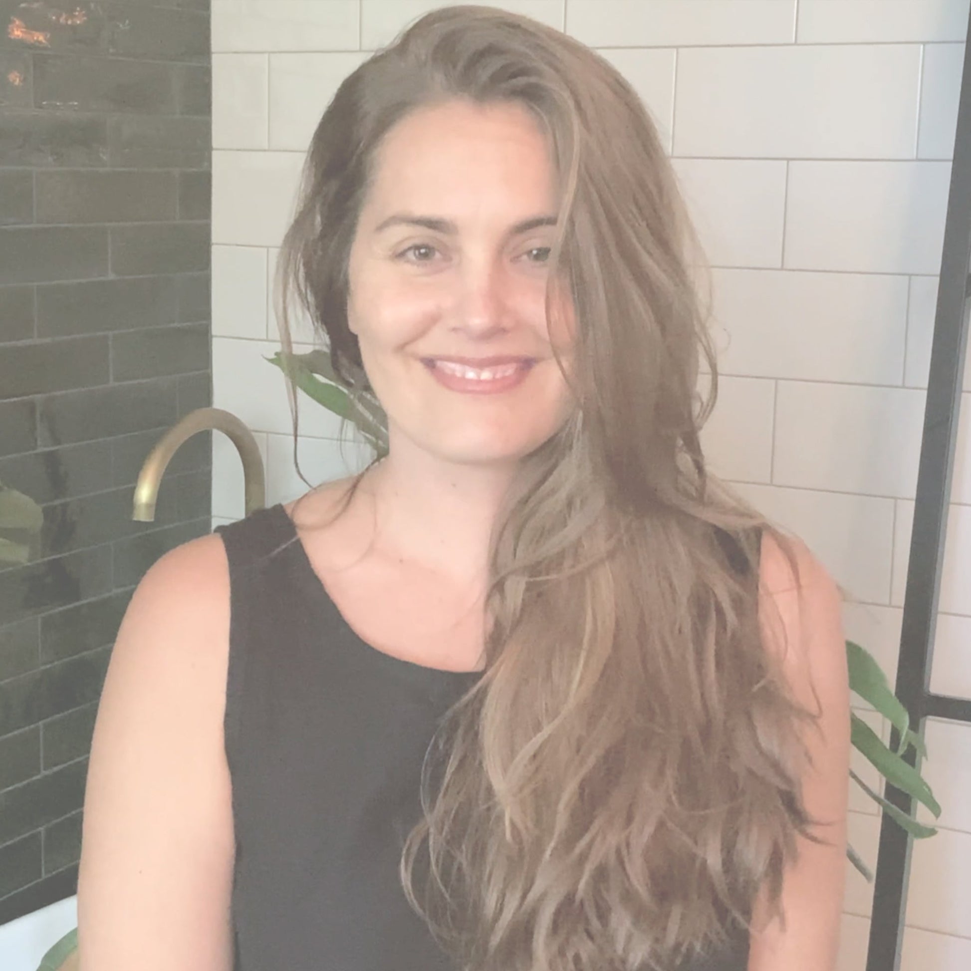 Video of Rachel Pachivas with long hair indoors explaining and demonstrating how to apply a smoothing hair serum for soft, manageable hair.