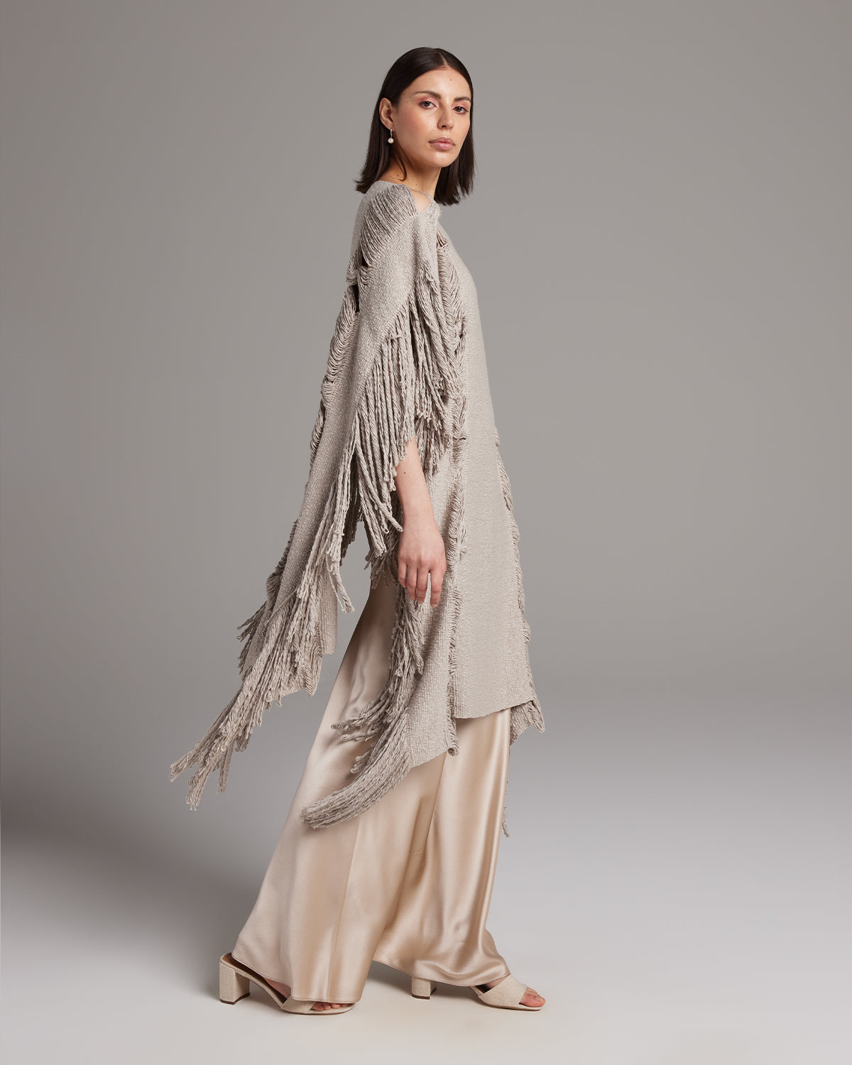 Model wearing a Lace Fringe Manta in taupe with fringed details, paired with a satin skirt.