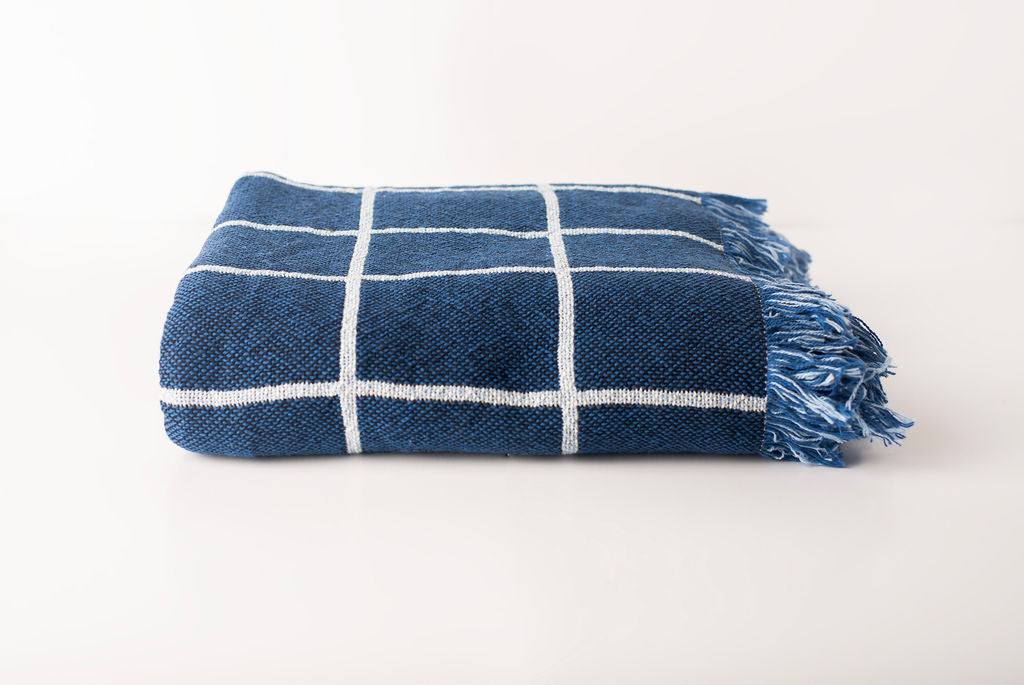 Front view of folded lapis blue and cream grid woven cotton throw on a white background