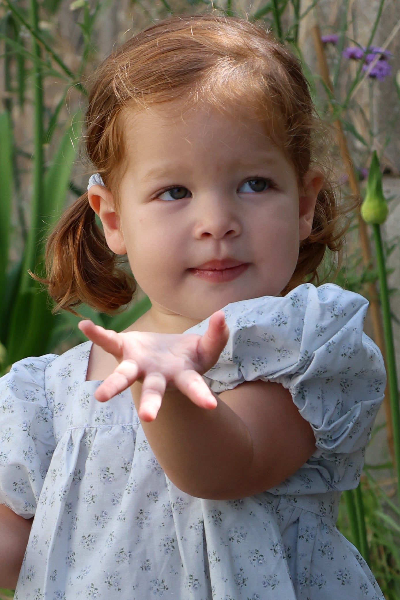 Young girl in a light blue dress holding out her hand in a garden setting