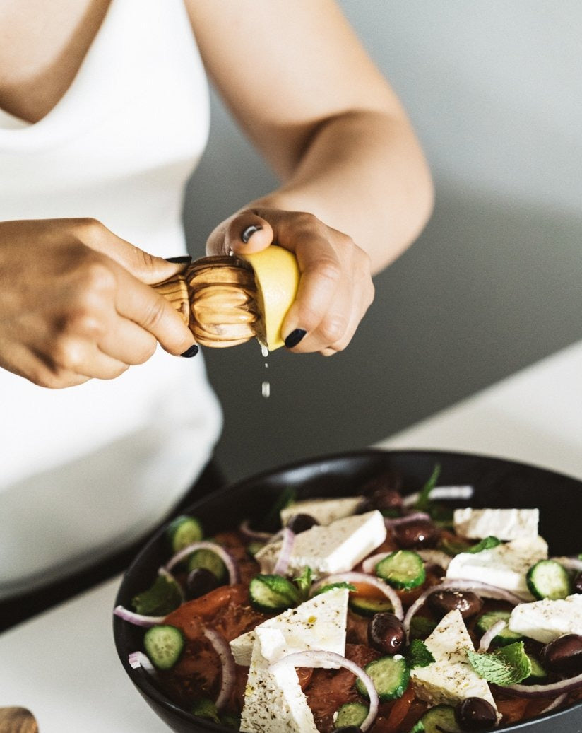 Person using a wooden lemon press to squeeze lemon juice over a bowl of salad on the table
