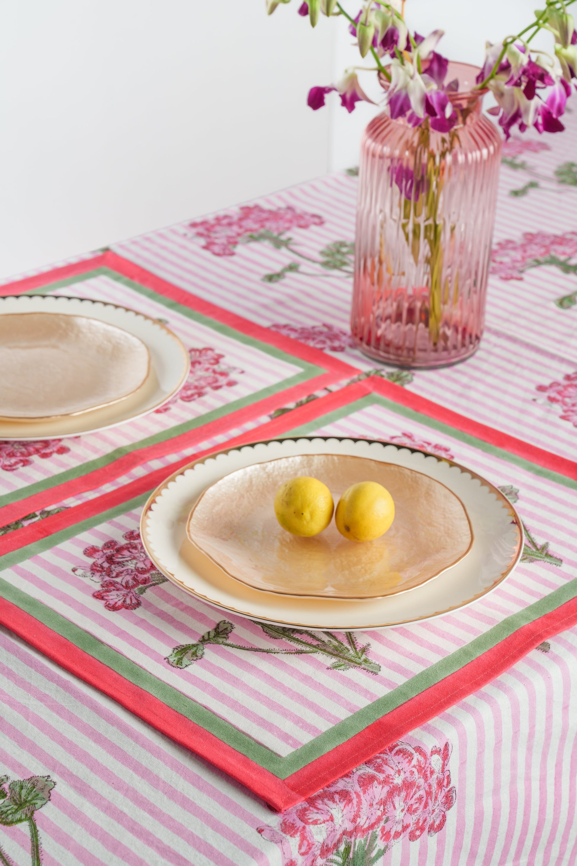 Pink hydrangea blockprint placemat with gold-rimmed plates and lemons on dining table