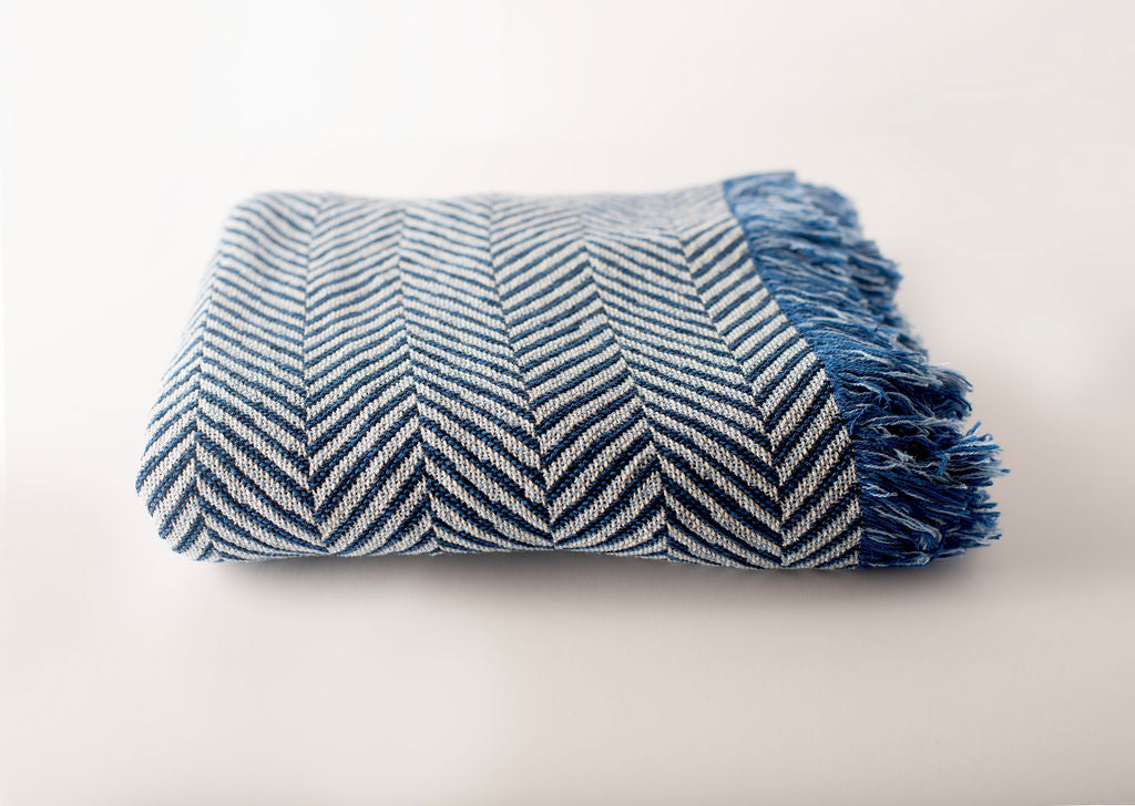Front view of folded blue and cream herringbone woven cotton throw on a white background