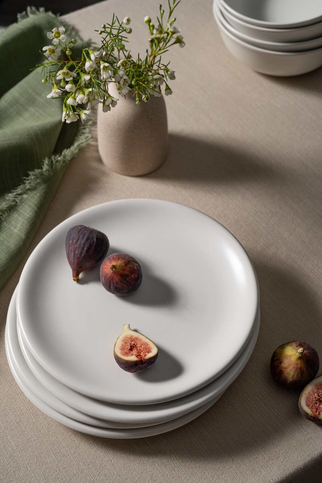 Bone-colored ceramic plates from Hamkke Home stacked on a linen tablecloth, styled with fresh figs for a minimal food photography look.