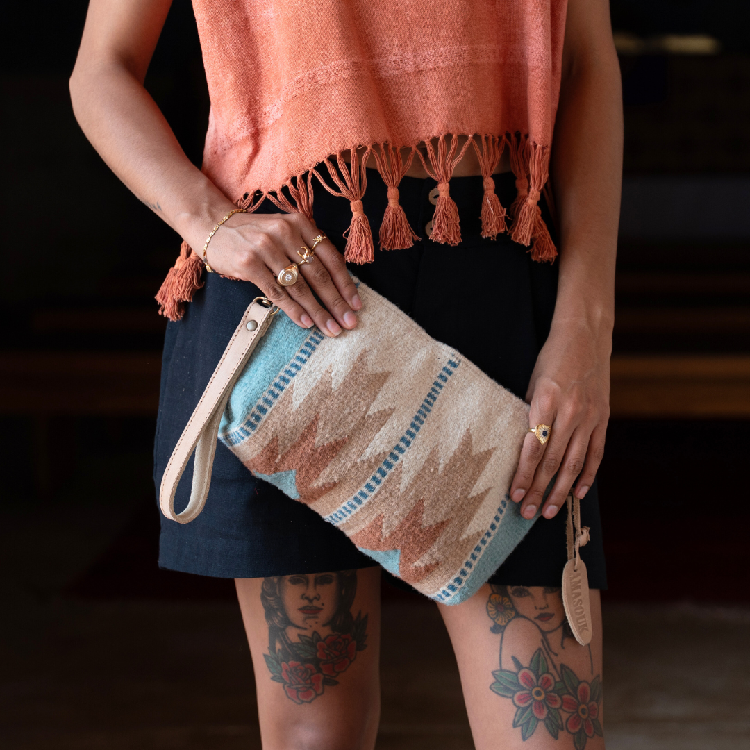 Woman wearing handwoven convertible clutch with Zapotec lightning design in rose and blue tones; functions as a pouch, wristlet, or crossbody with leather straps and internal pocket