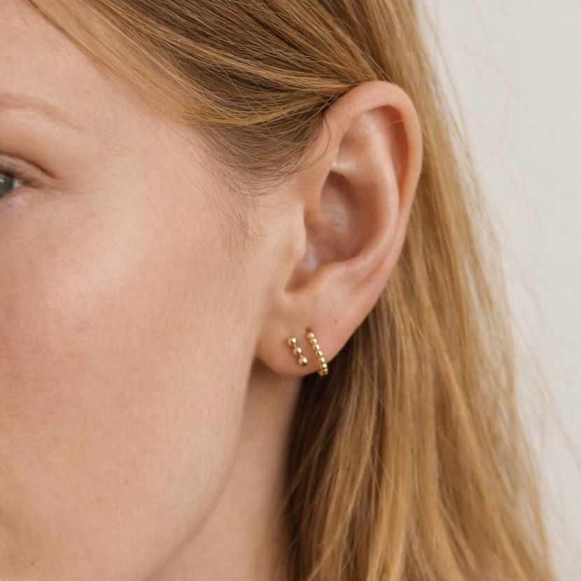 Close-up of a person wearing gold earrings with a neutral background