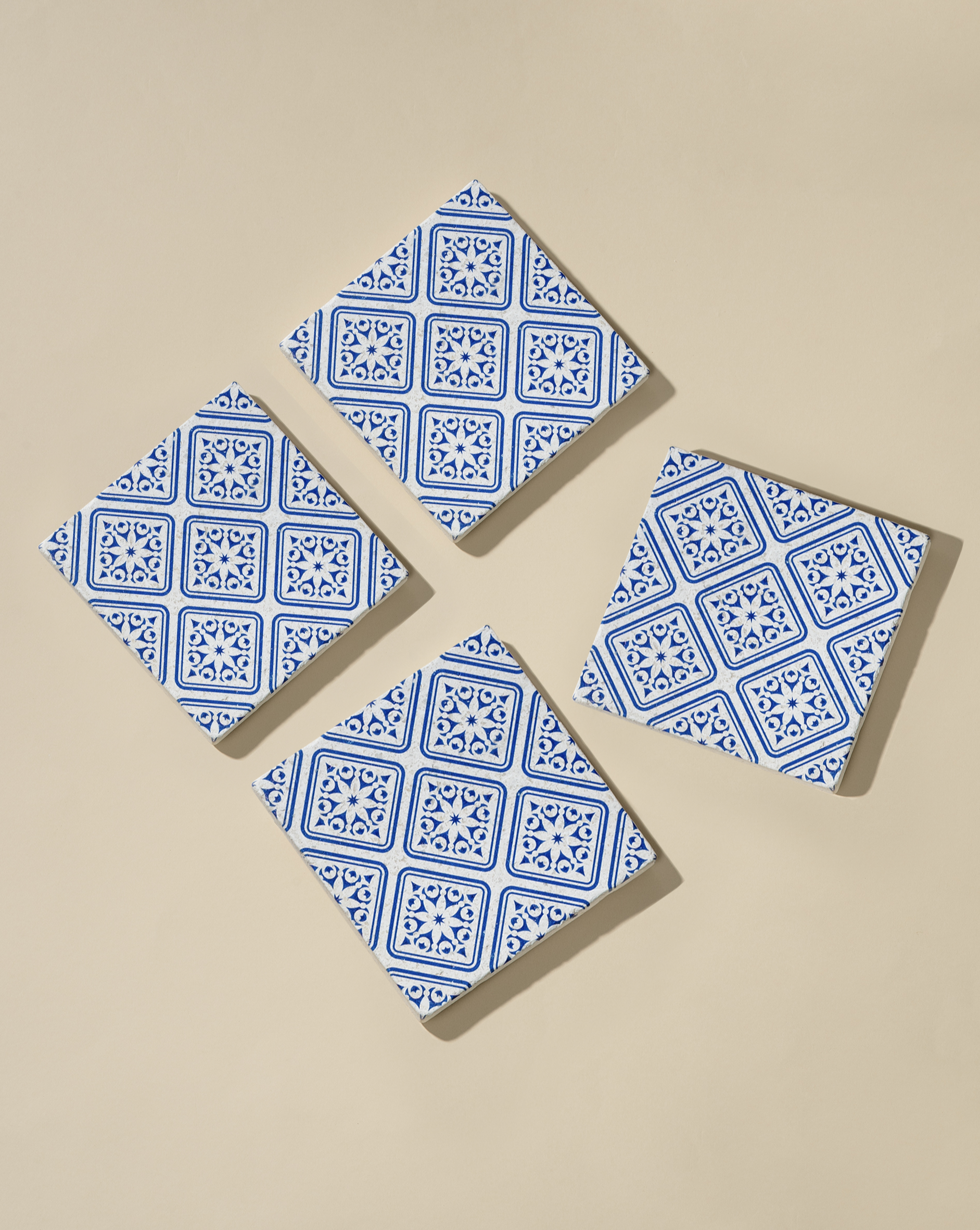 A set of four square white marble coasters with blue geometric patterns, displayed on a neutral background.