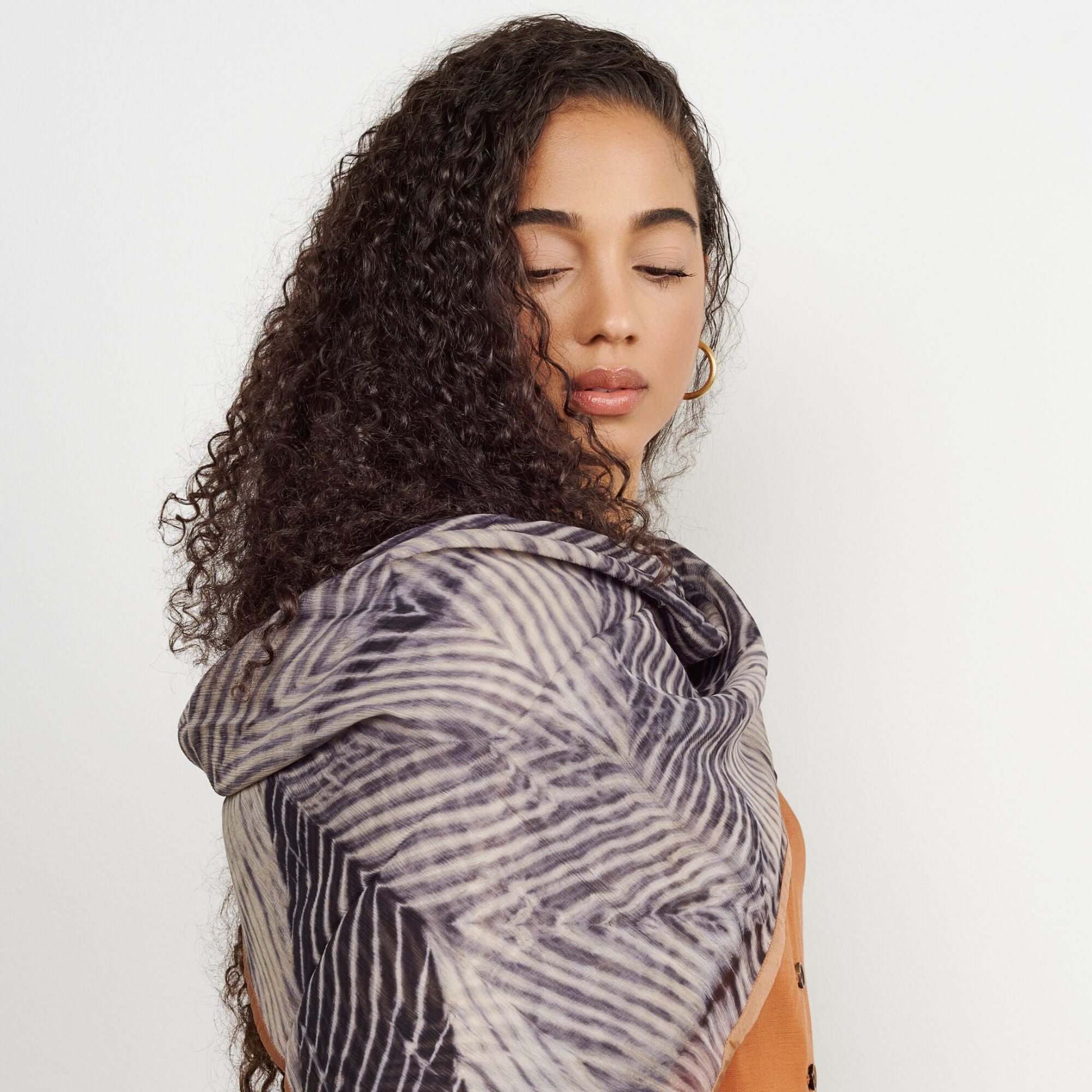 Chiffon square scarf Samu Black hand crafted shibori print silk worn elegantly by a woman with curly hair.
