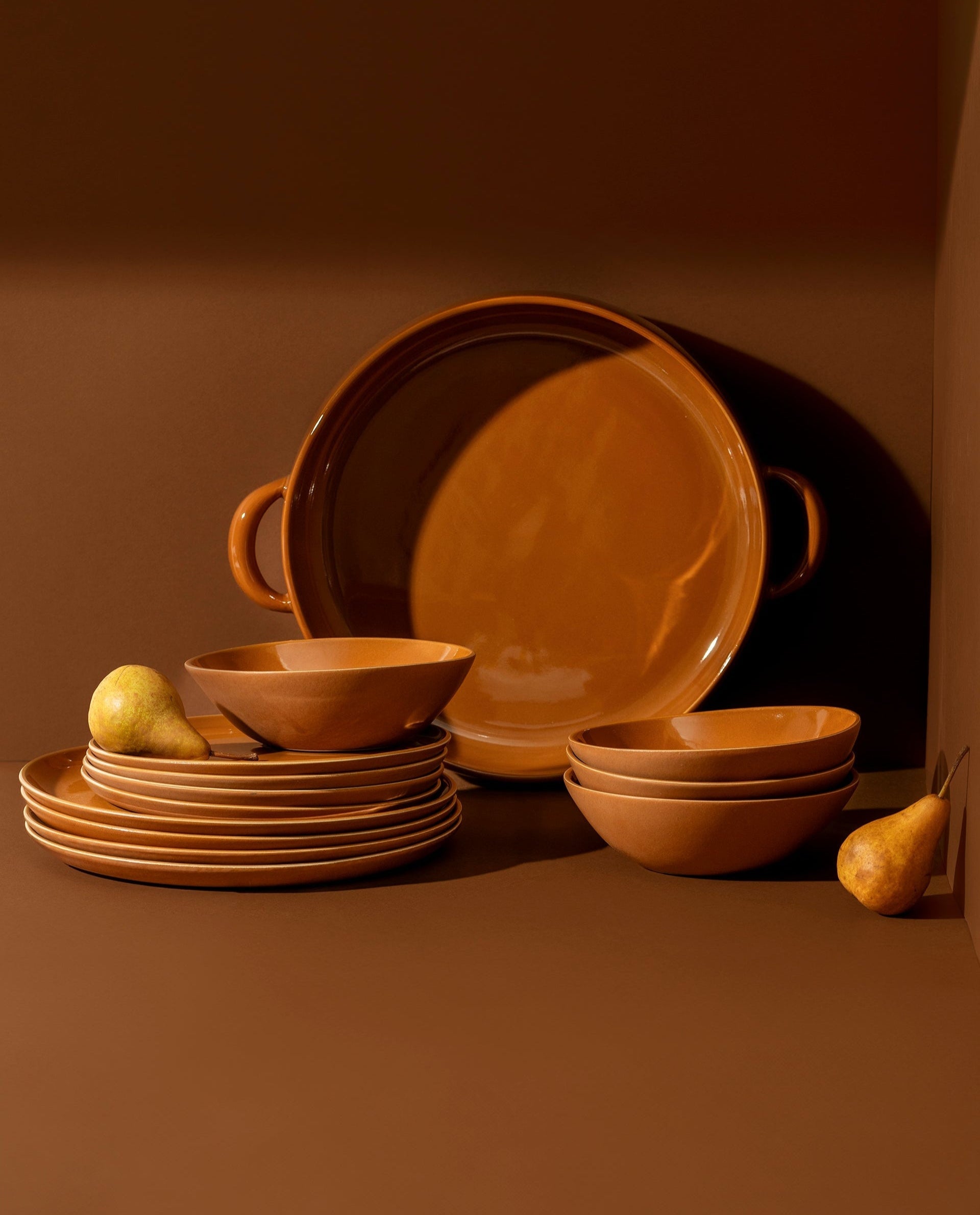 A set of white stoneware dinnerware including flat round dinner plates, flat round salad plates, organic-shaped soup bowls, and a large plate with handles.