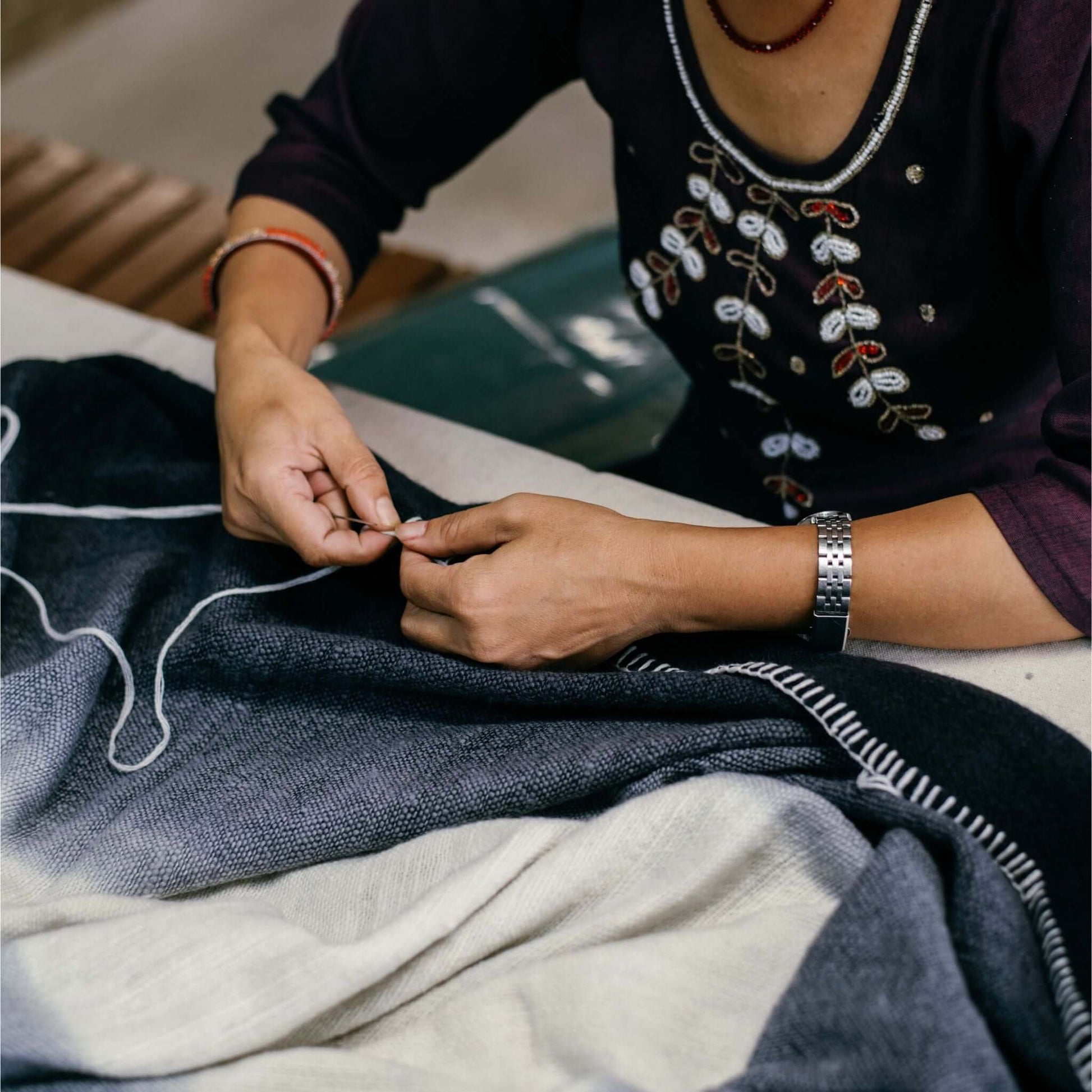 Artisan hand stitching the Ink Black White Ombre Textured Throw In Hand Spun Merino And Hand Stitched Hem.