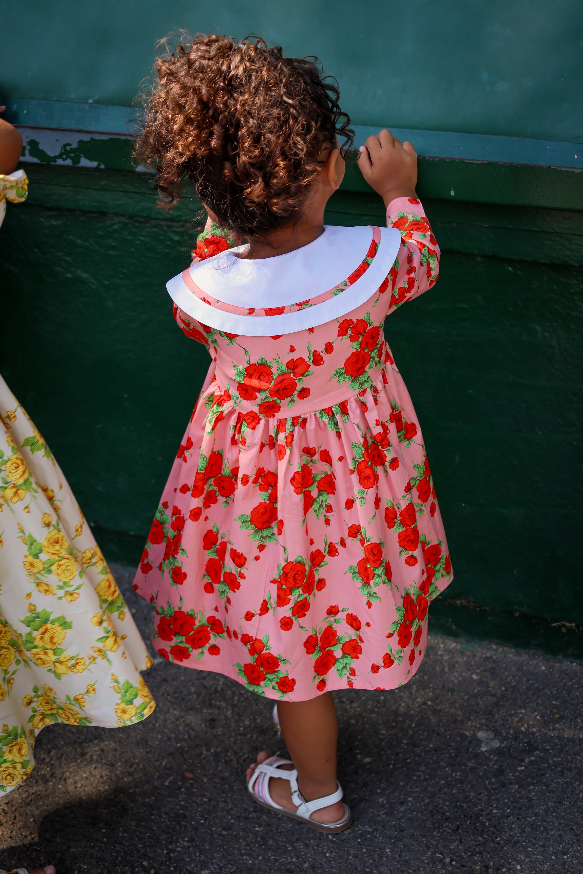 Child wearing a pink floral dress standing next to a green wall.