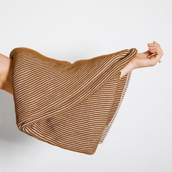 Copper and brown textured throw blanket folded and draped over a person's arm on a white background.
