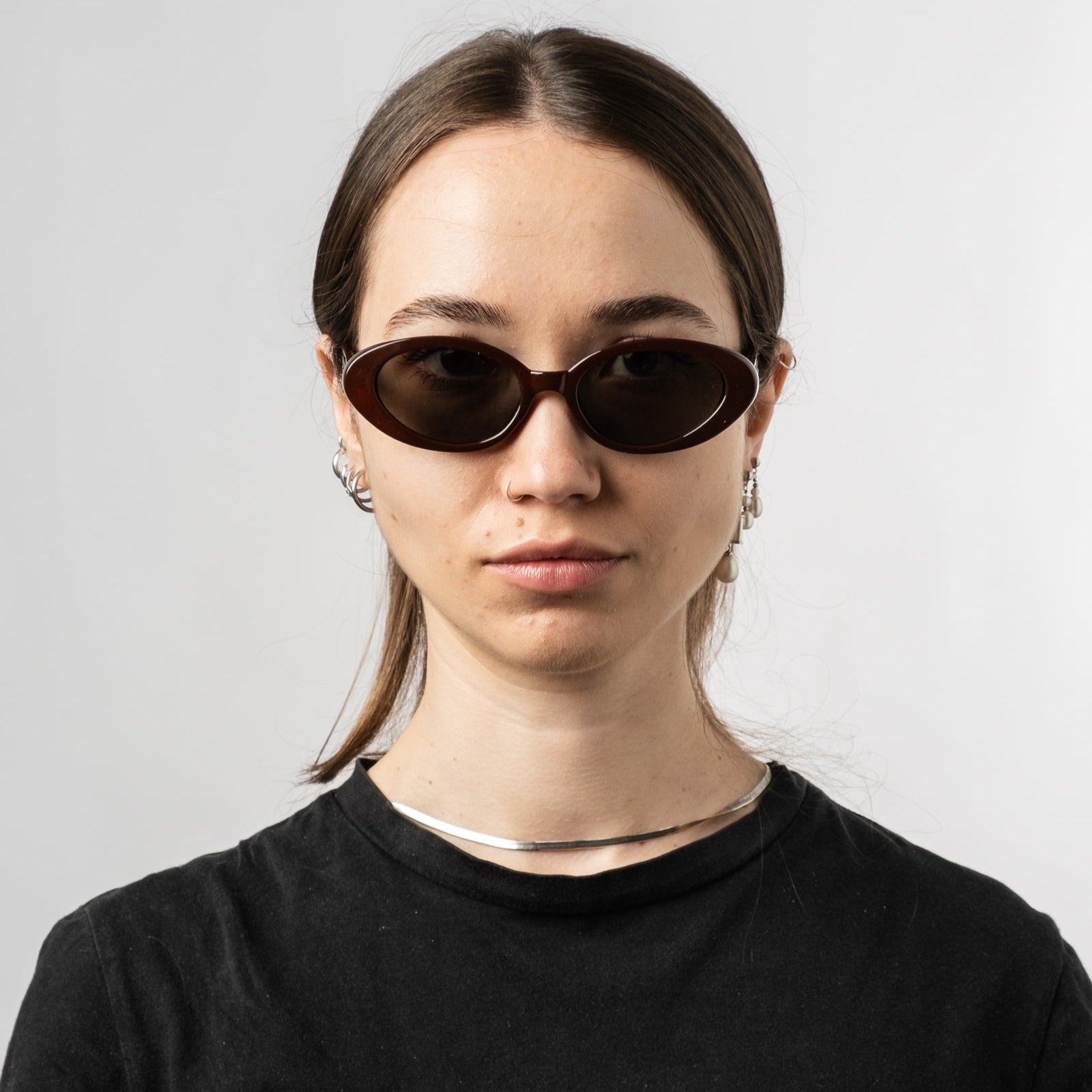 Female wearing Sad Eyewear Bloom oval sunglasses in tobacco red with tinted black lenses