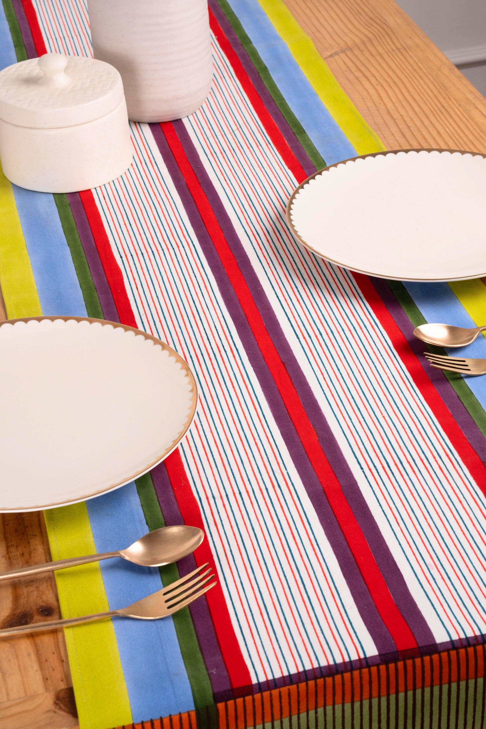 Modernist striped tablerunner with white plates and gold utensils on wooden table