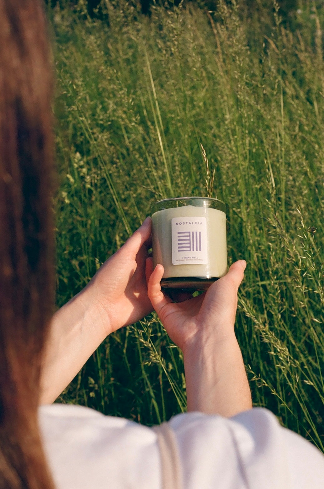 Person holding a candle with a brand label in a grassy field