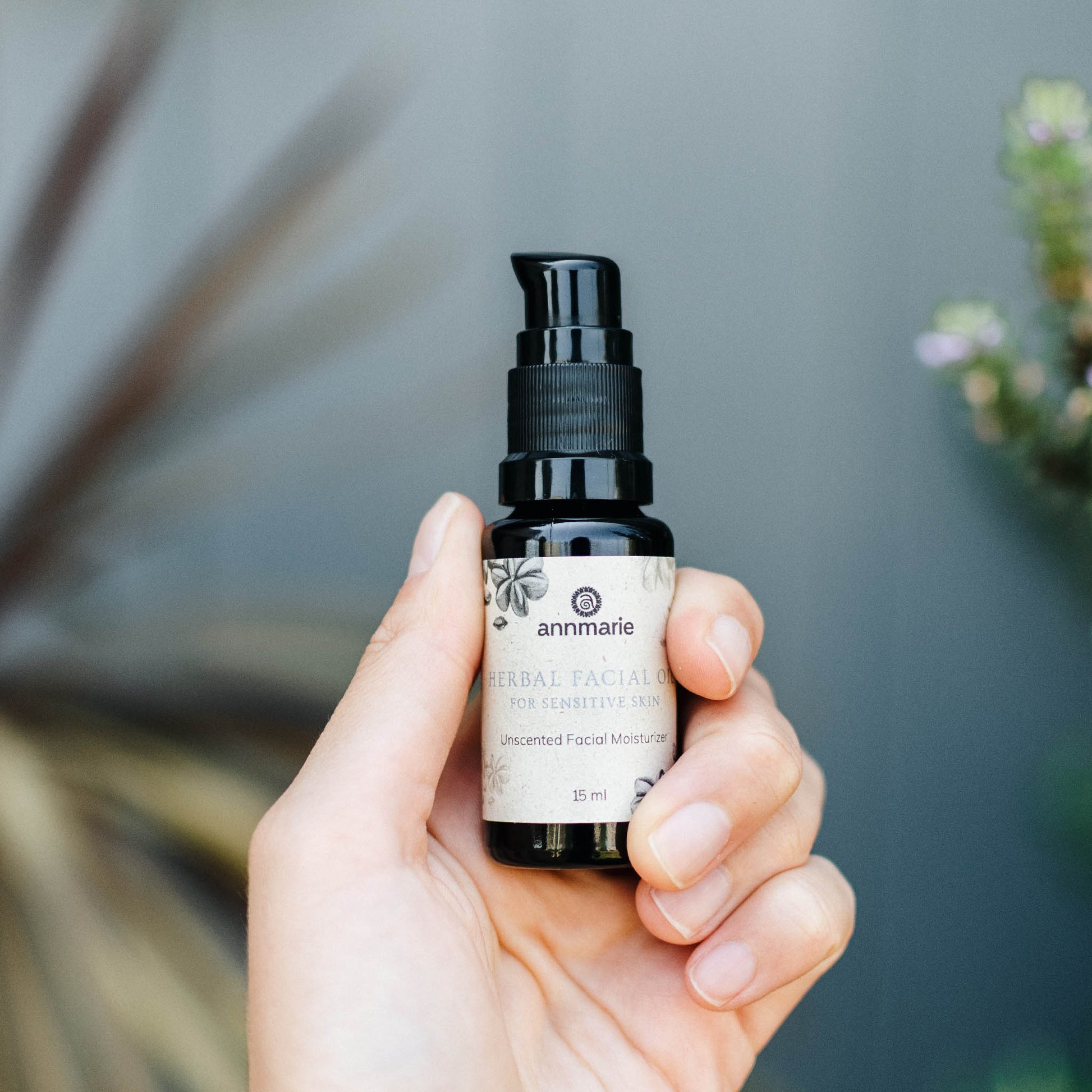 Hand holding Annmarie Herbal Facial Oil for Sensitive Skin unscented facial moisturizer in a small pump bottle.