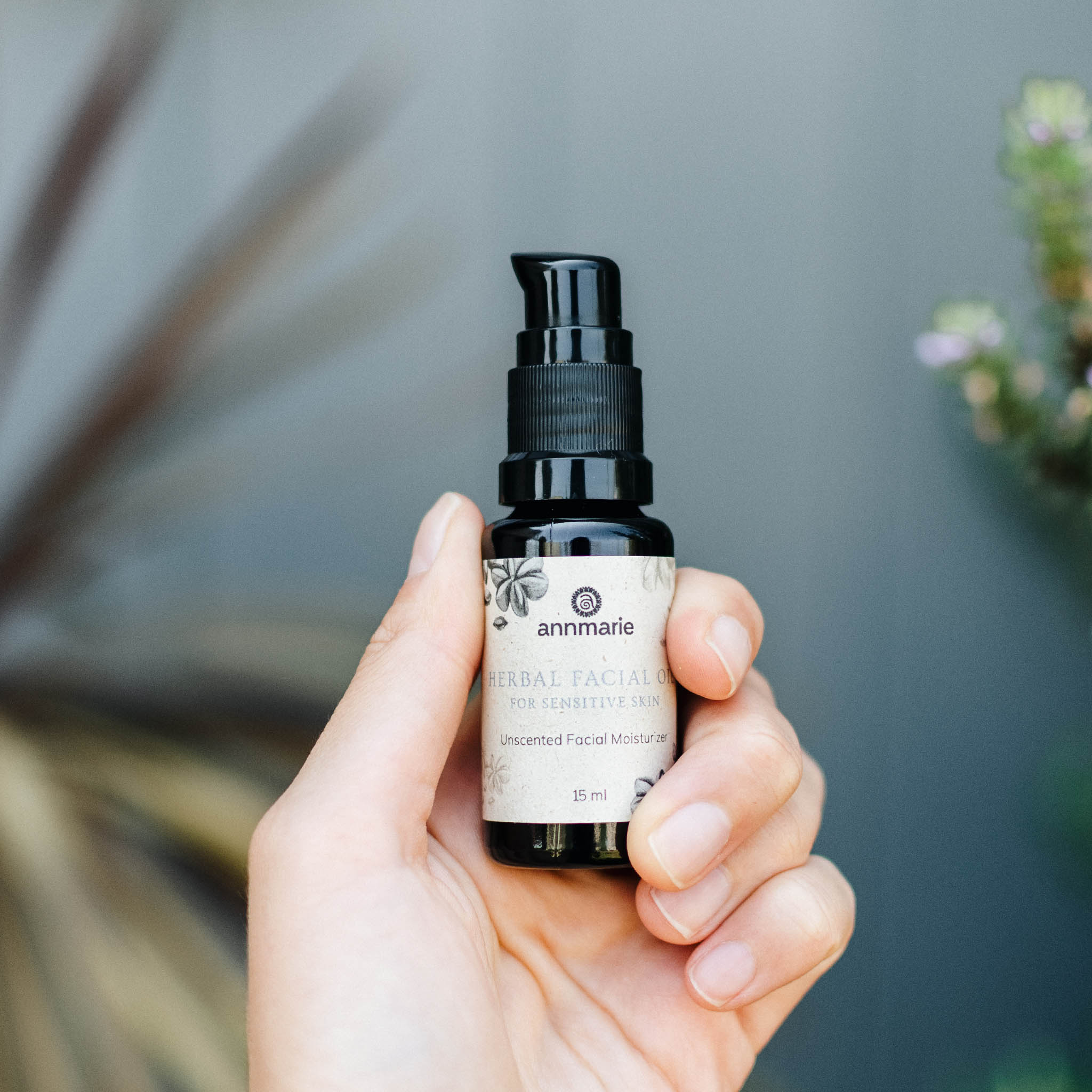 Hand holding Annmarie Herbal Facial Oil for Sensitive Skin unscented facial moisturizer in a small pump bottle.