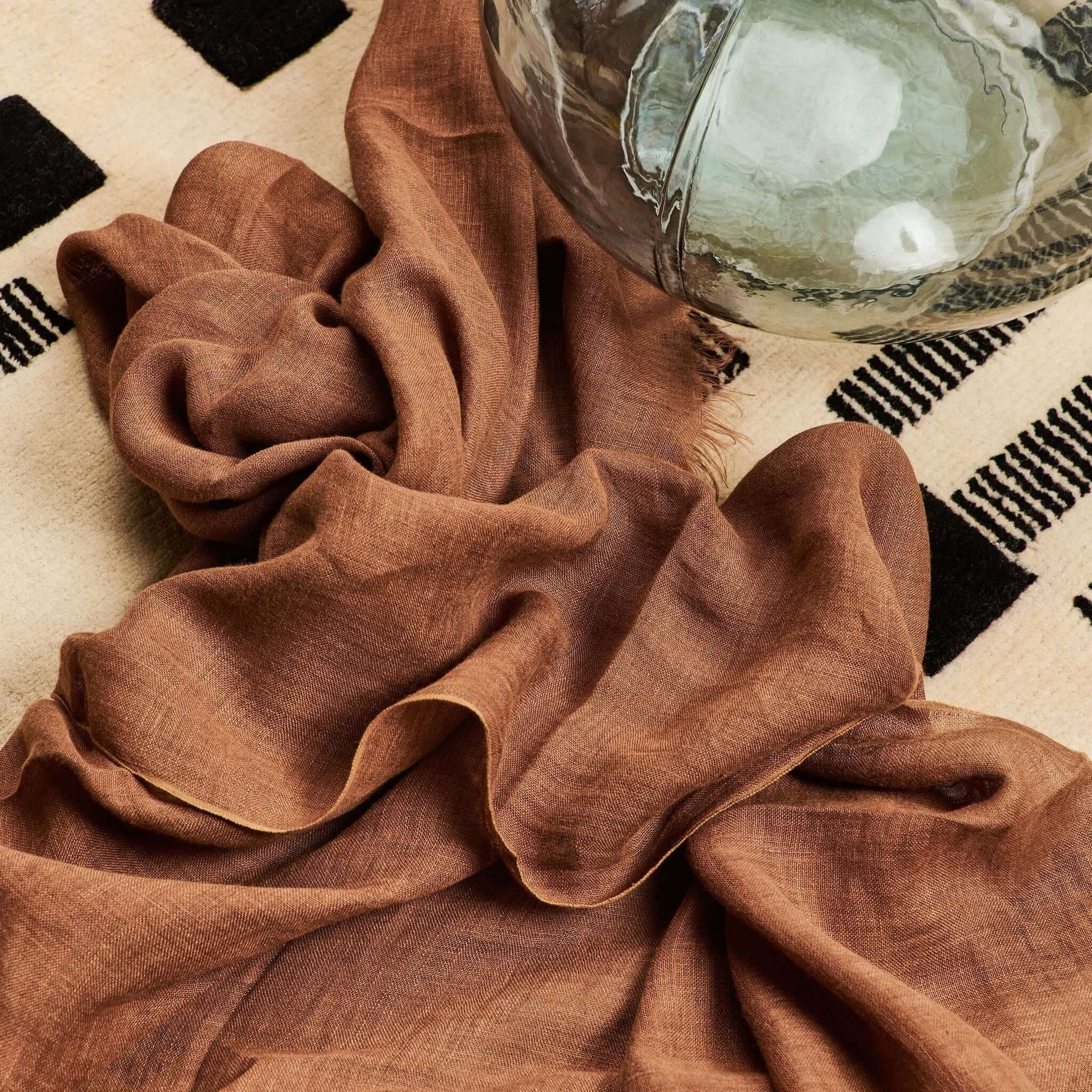 Coco Brown Hand Woven Linen Silk Blend Scarf draped elegantly on a textured surface with a decorative glass bowl.