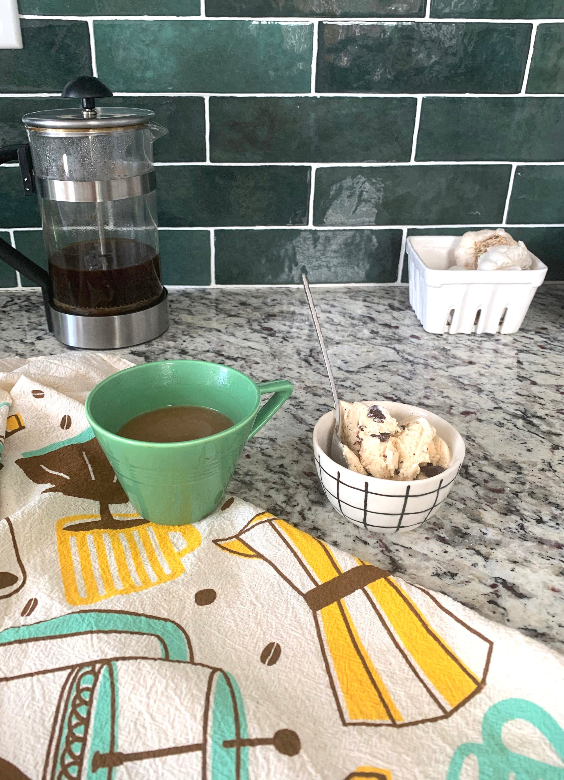 Coffee dish towel on kitchen counter next to a cup of coffee and bowl of ice cream.