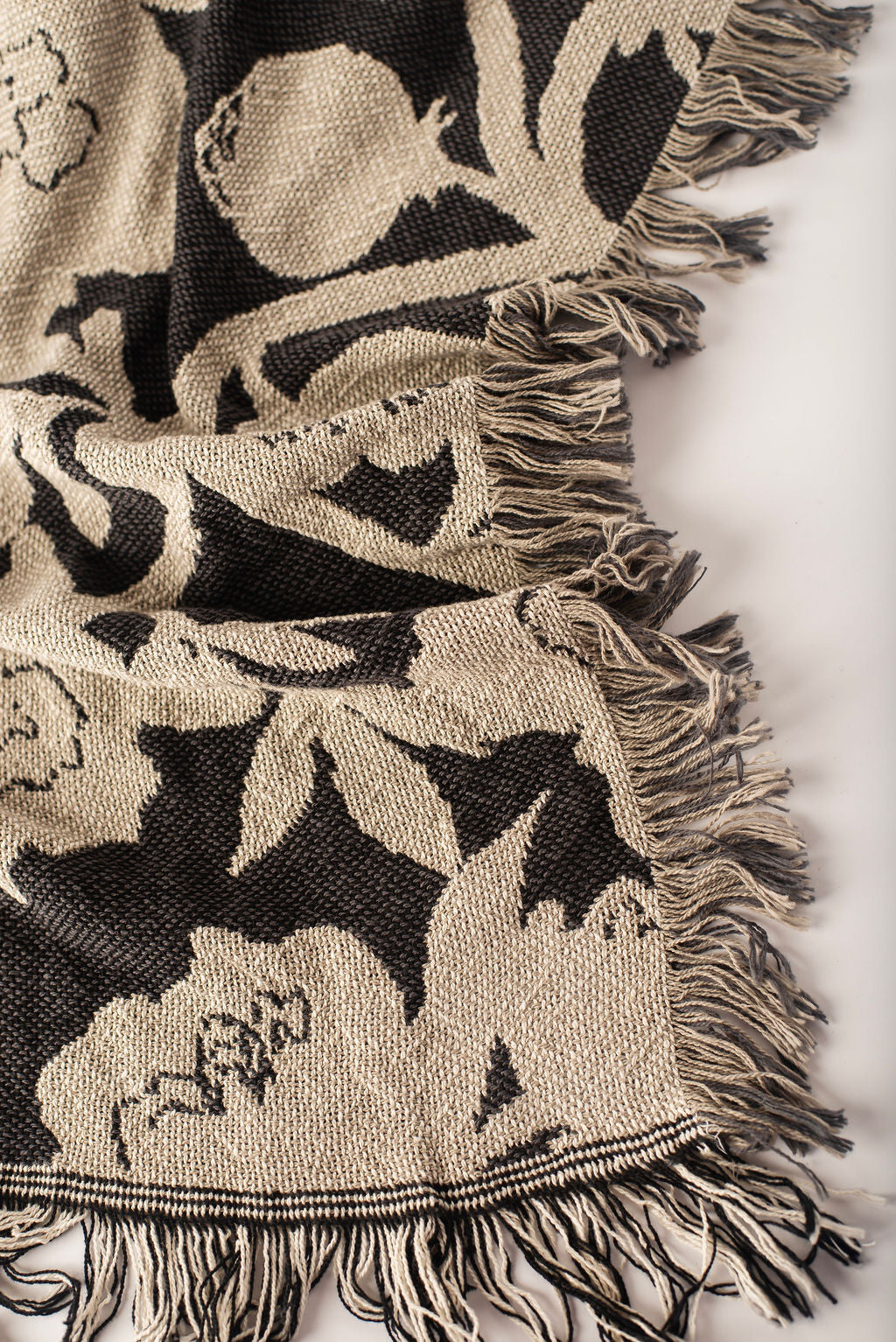 Close-up of Addy Tuffet charcoal, taupe, and cream floral woven cotton throw with fringe