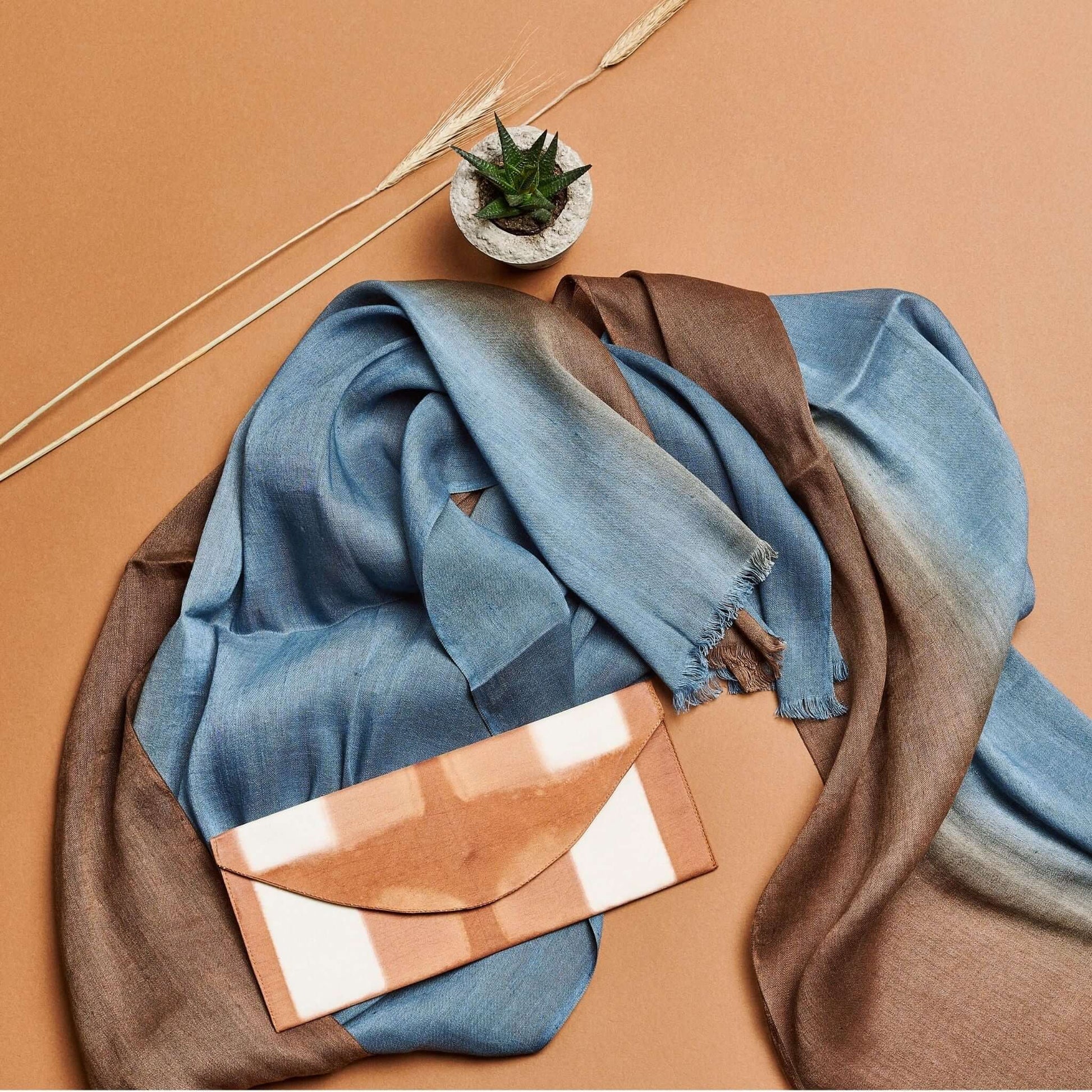 Mahogany Sky Brown Blue Ombre Linen Silk Handloom Scarf draped with a stylish clutch on a beige background.