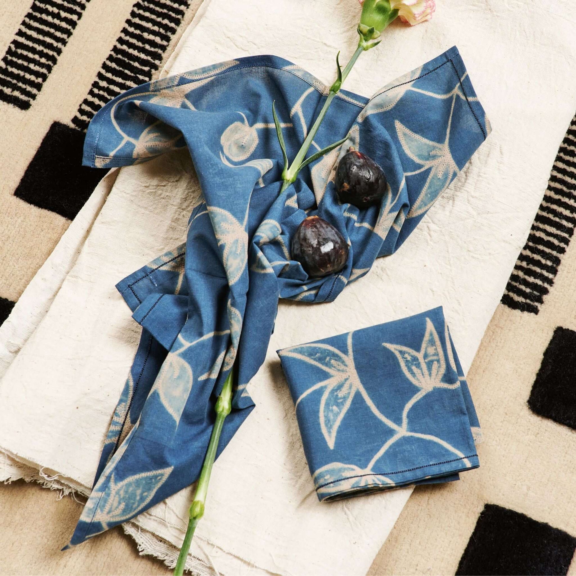Folio Indigo Handcrafted Shibori Cotton Table Napkins ( set of 4 ) elegantly displayed with flowers on a textured table.