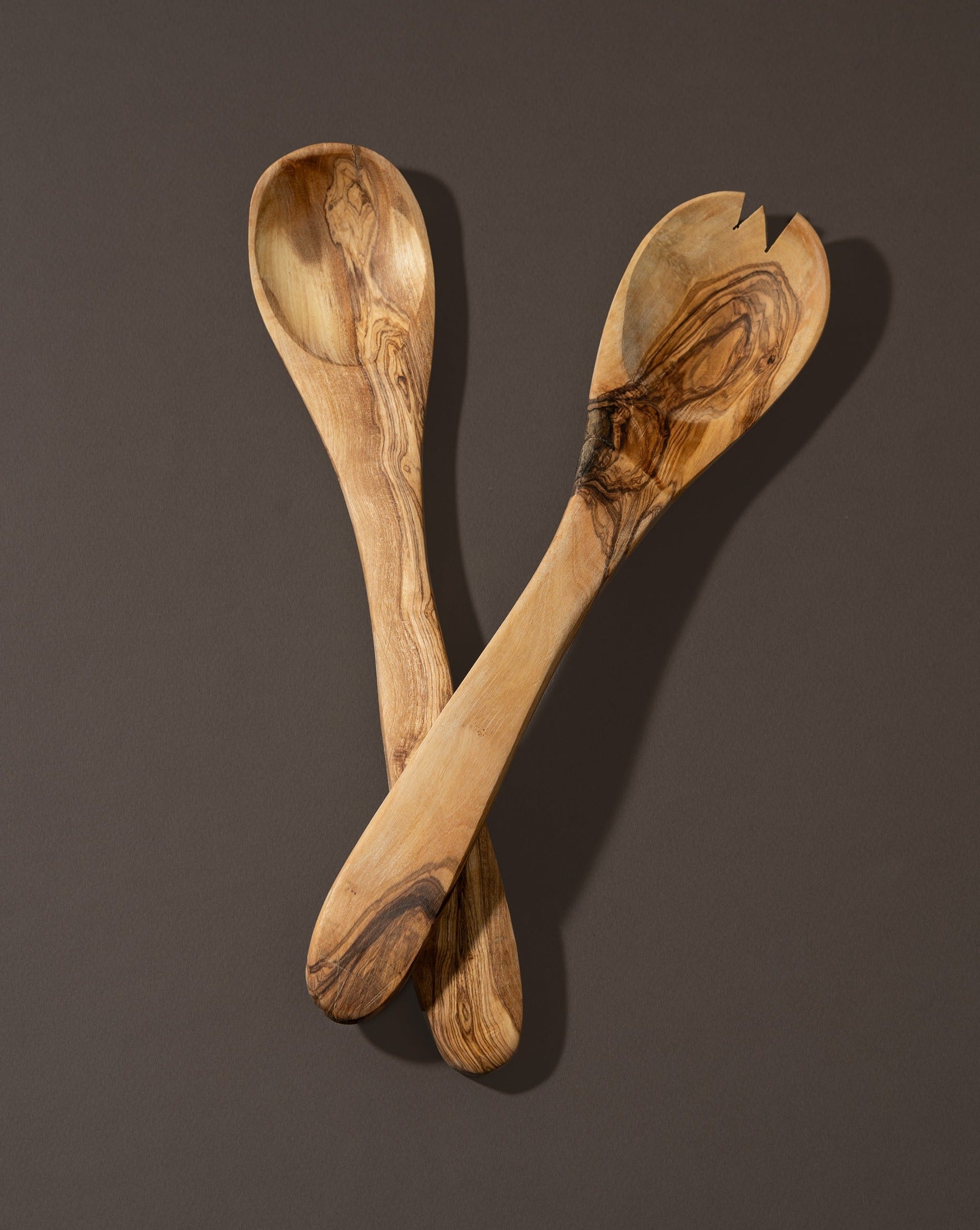 A pair of olive wood utensils, likely a spoon and fork, laid on a dark surface.