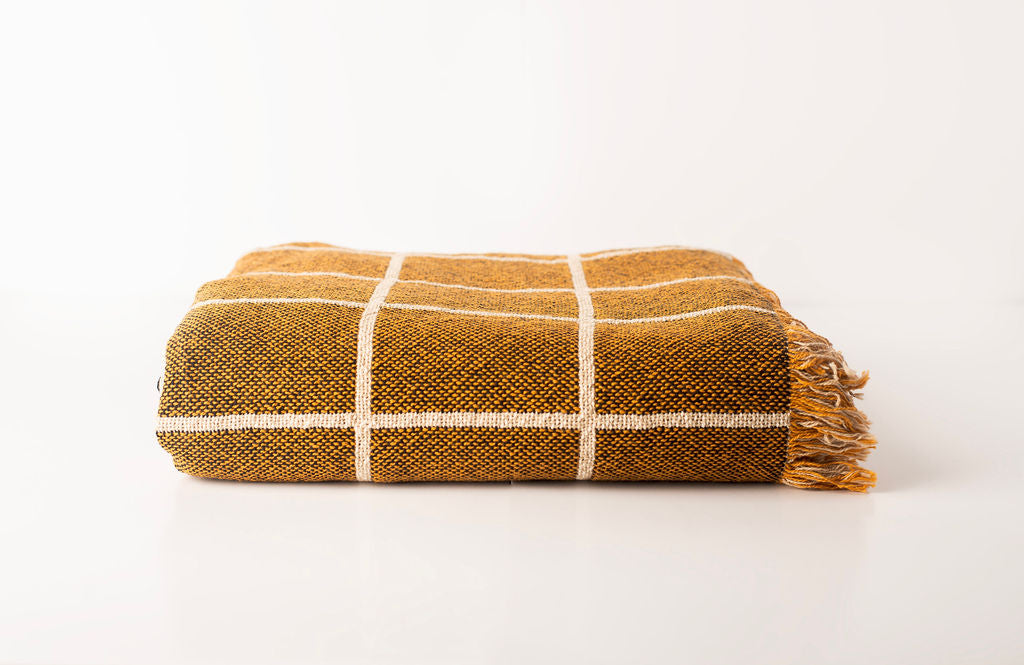 Front view of folded golden brown and cream grid woven cotton throw on a white background