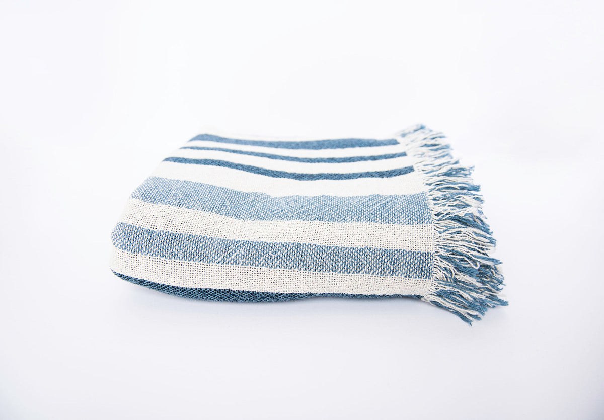 Side view of folded blue and cream coastal stripe woven cotton blanket