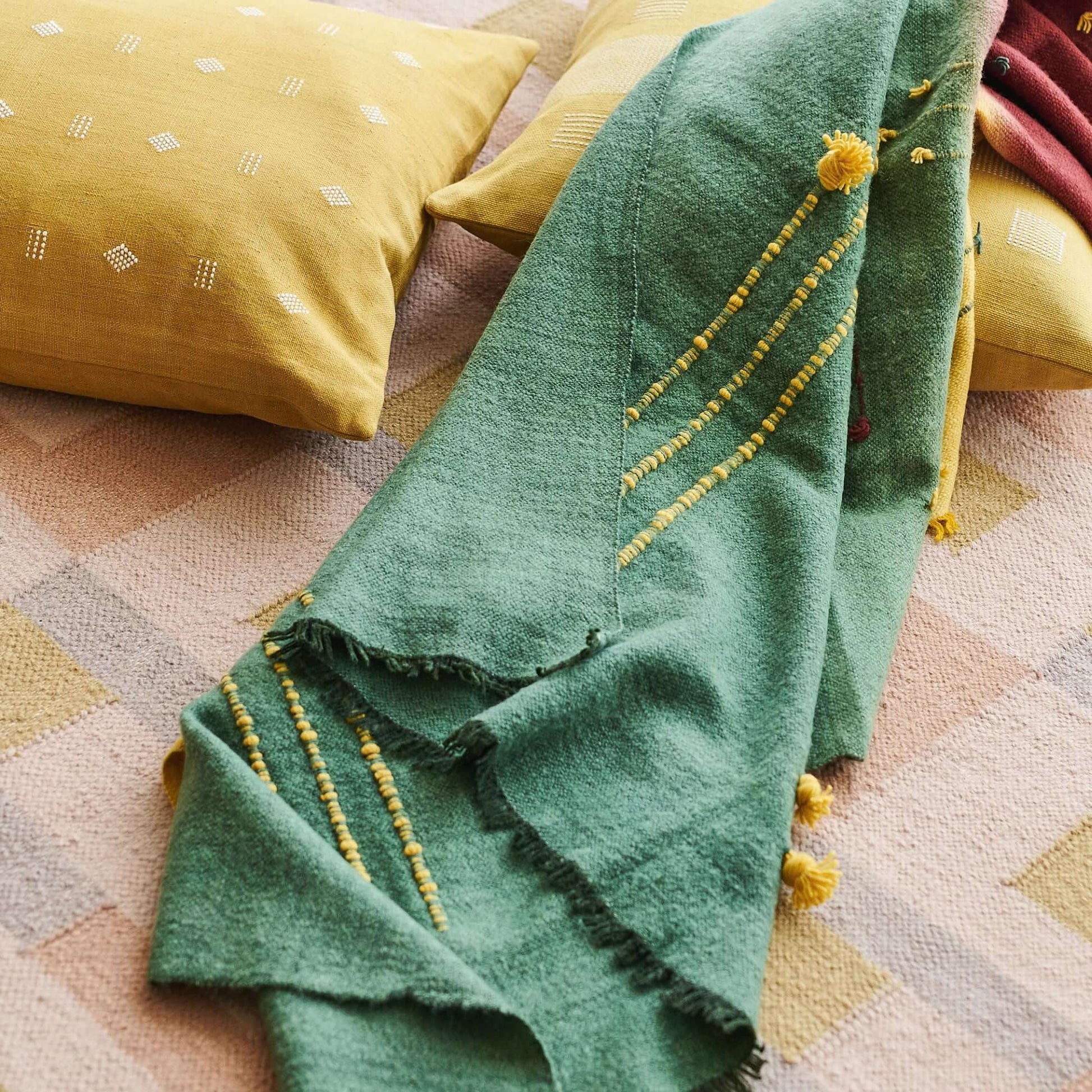 Avocado Green Multi Color Warm Hues Hand Woven Hand Knotted Textured Merino Throw draped over patterned cushions.