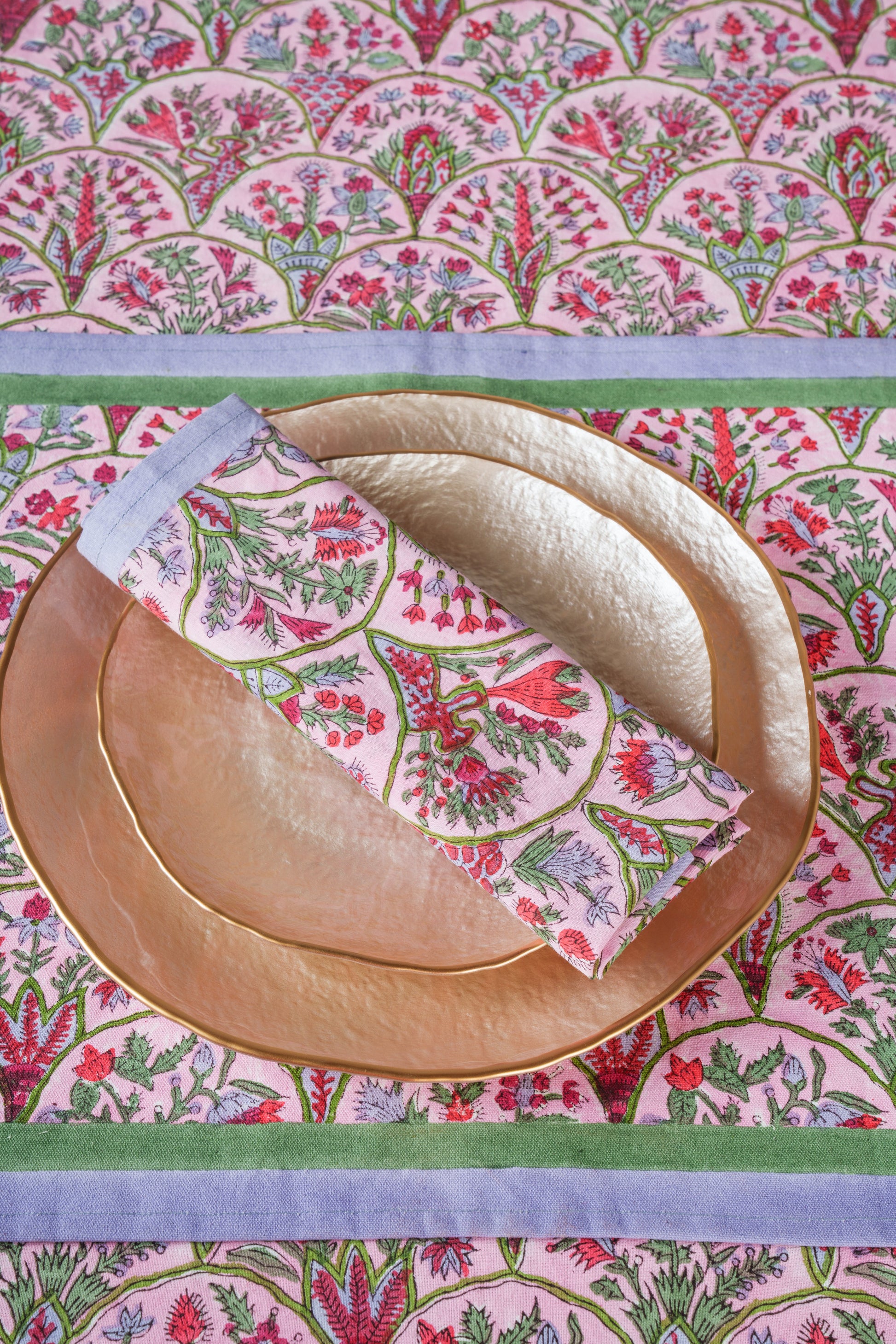 Pink arch blockprint napkin folded on gold plate with matching design
