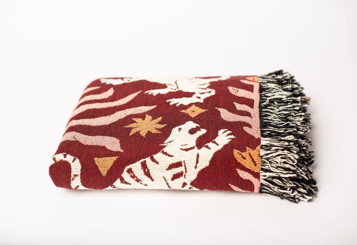 Close-up of Leona Solstice red, coral, cream, and gold tiger folk-art jacquard woven blanket with fringe