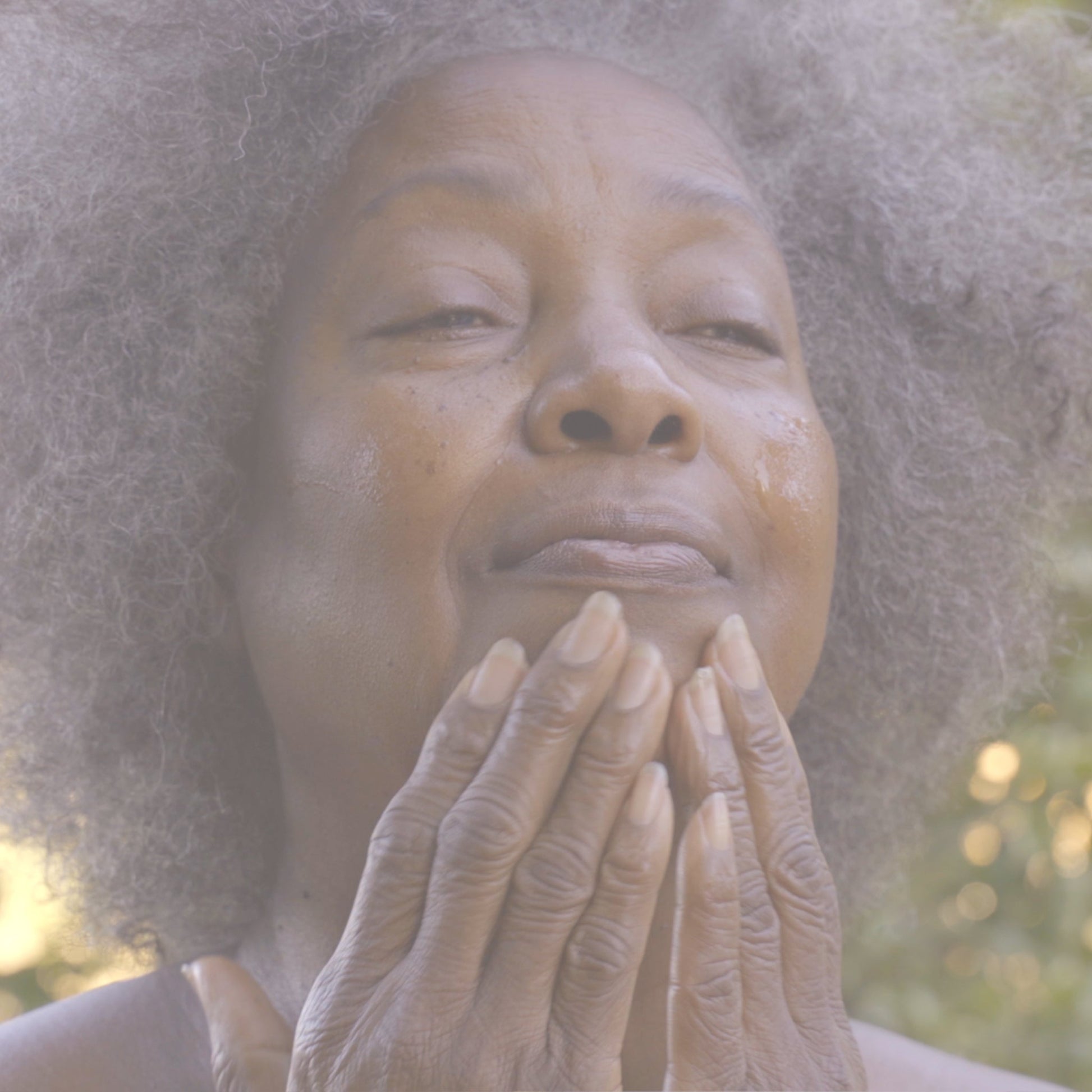 Video of woman gently applying facial serum to her cheeks and chin with both hands during a skincare routine outdoors.