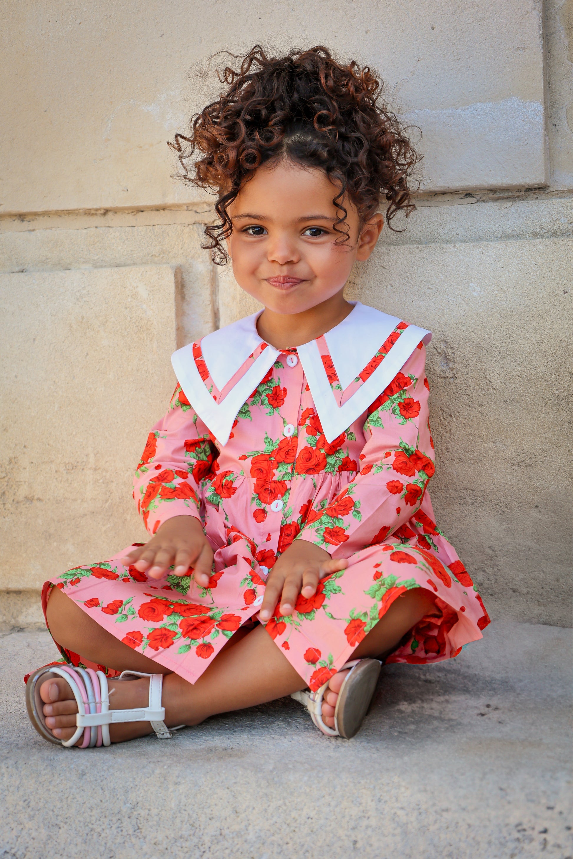 Young girl in a floral dress sitting on steps.