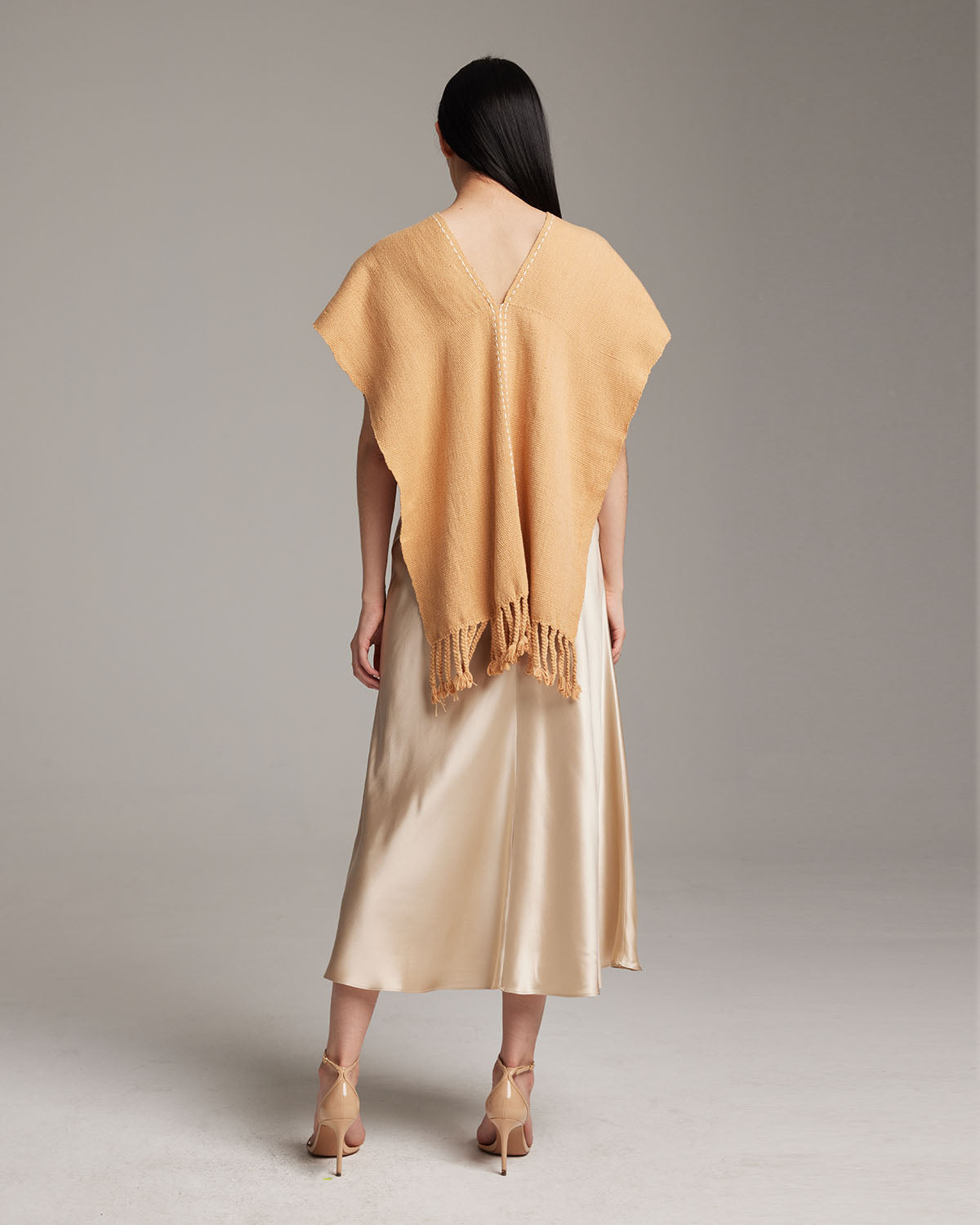 Model wearing a copper threads manta in apricot color, showcasing the back and fringe detail.