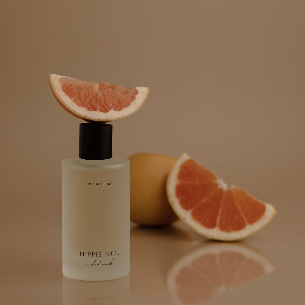 Bottle of 'Hippie Soul' with a slice of grapefruit on a reflective surface against a brown background