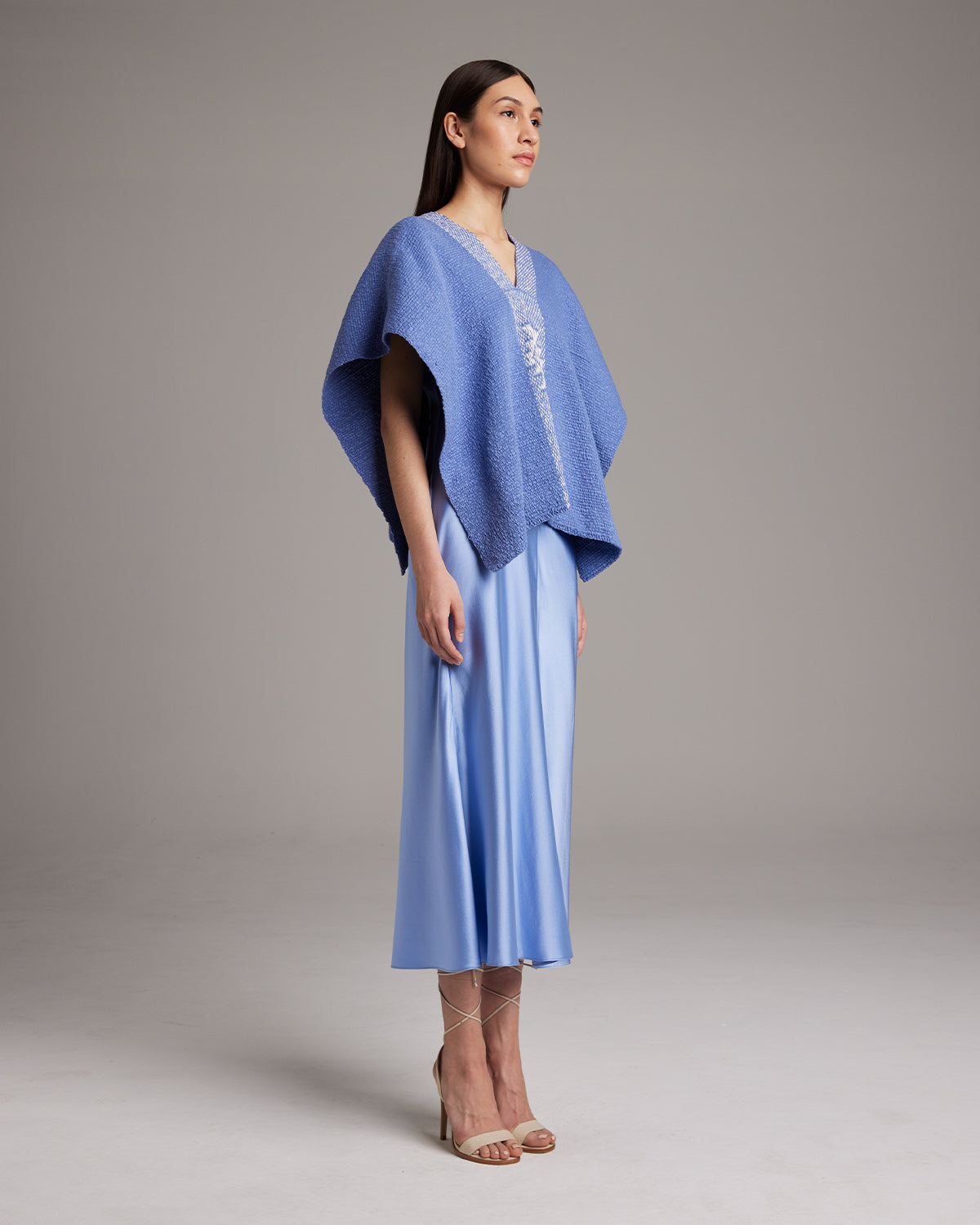 Model wearing a blue Manta Estrella poncho over a satin dress