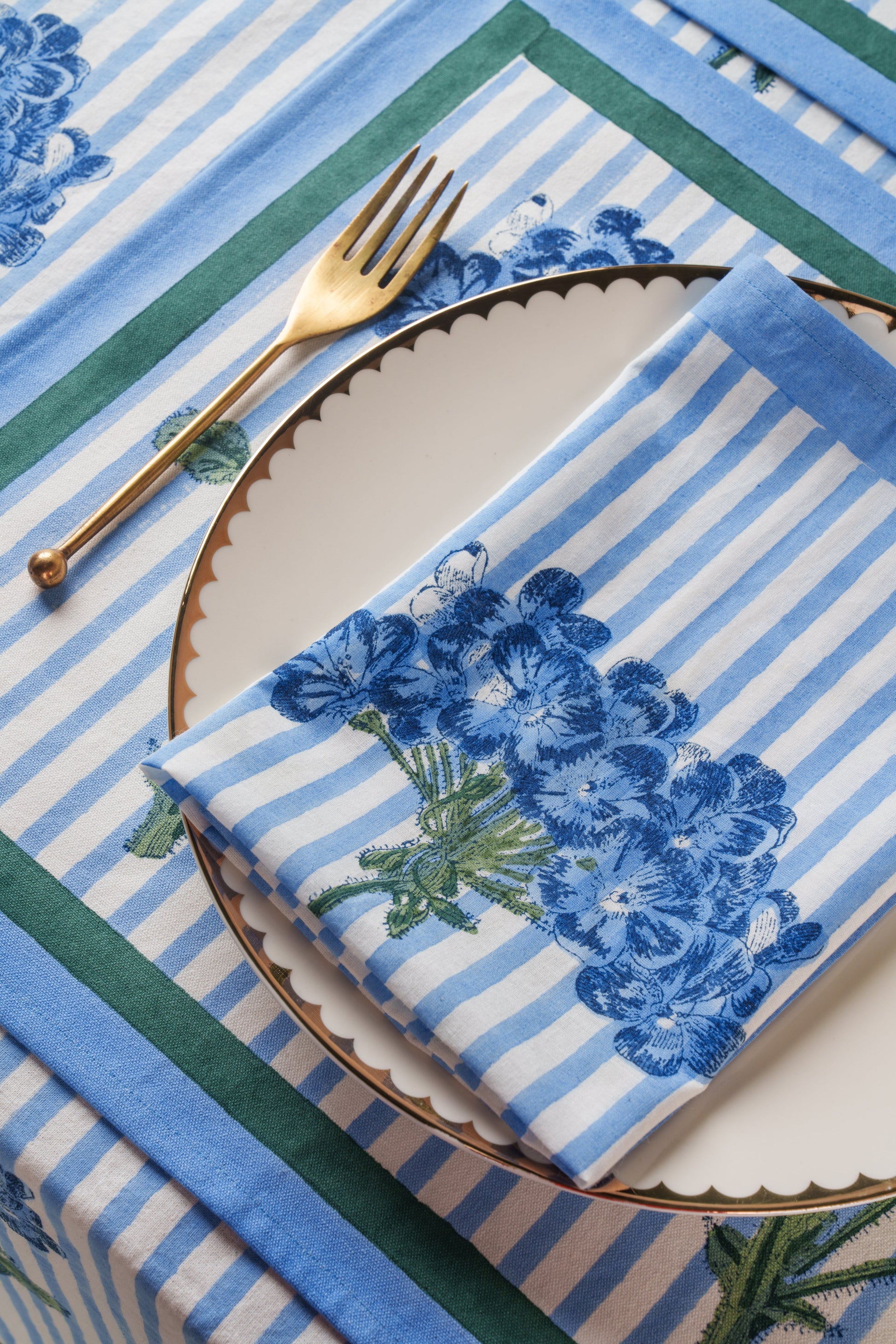 Blue hydrangea blockprint napkin folded on scalloped plate with gold fork, matching tablecloth