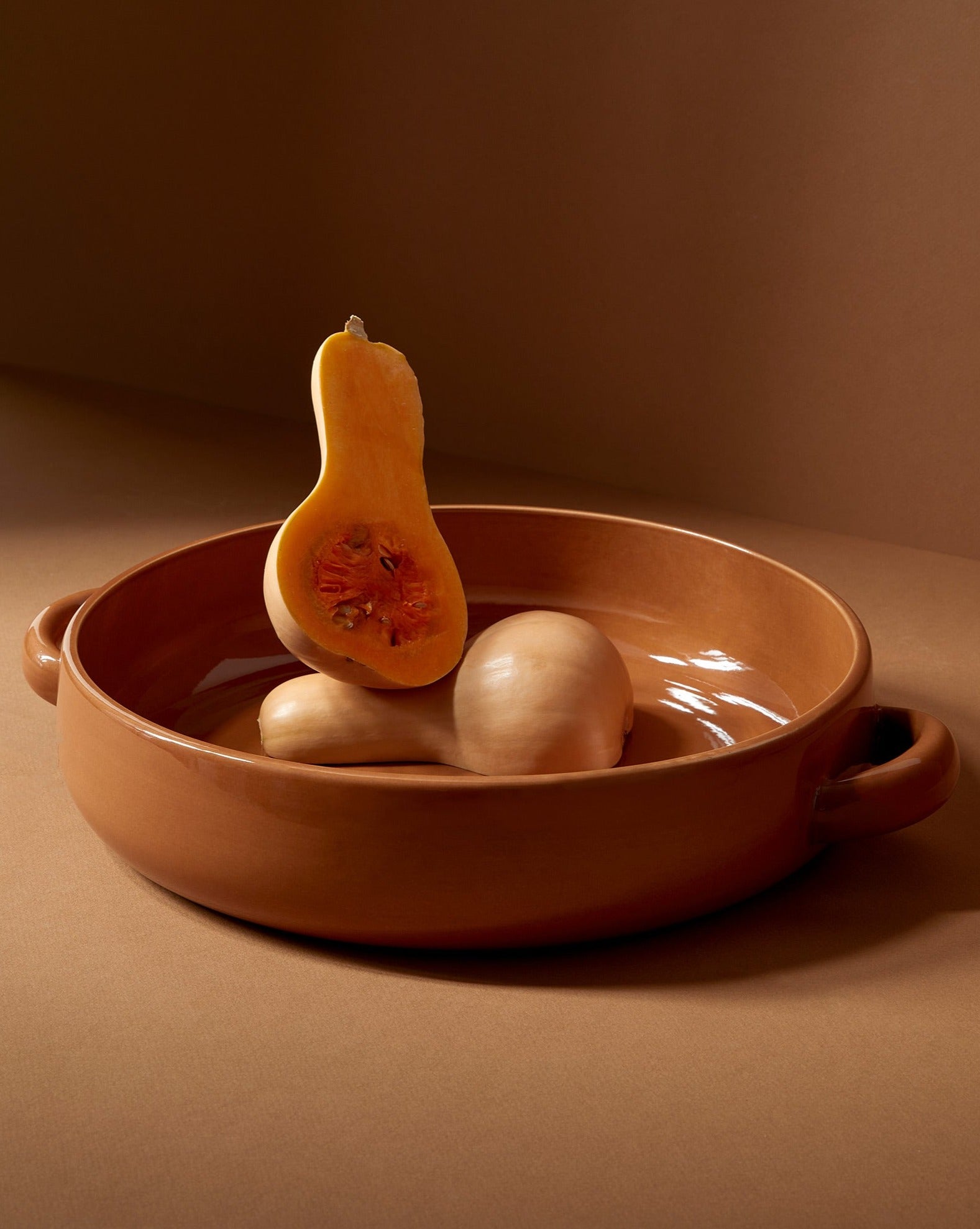 A white stoneware serving plate with handles, featuring a minimalist design, displayed with a piece of cauliflower on it, set against a neutral background.