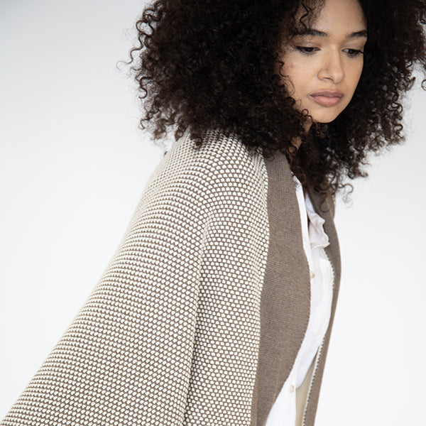 Woman wearing a textured beige throw blanket with a dotted pattern and dark brown border over a white shirt on a light background.