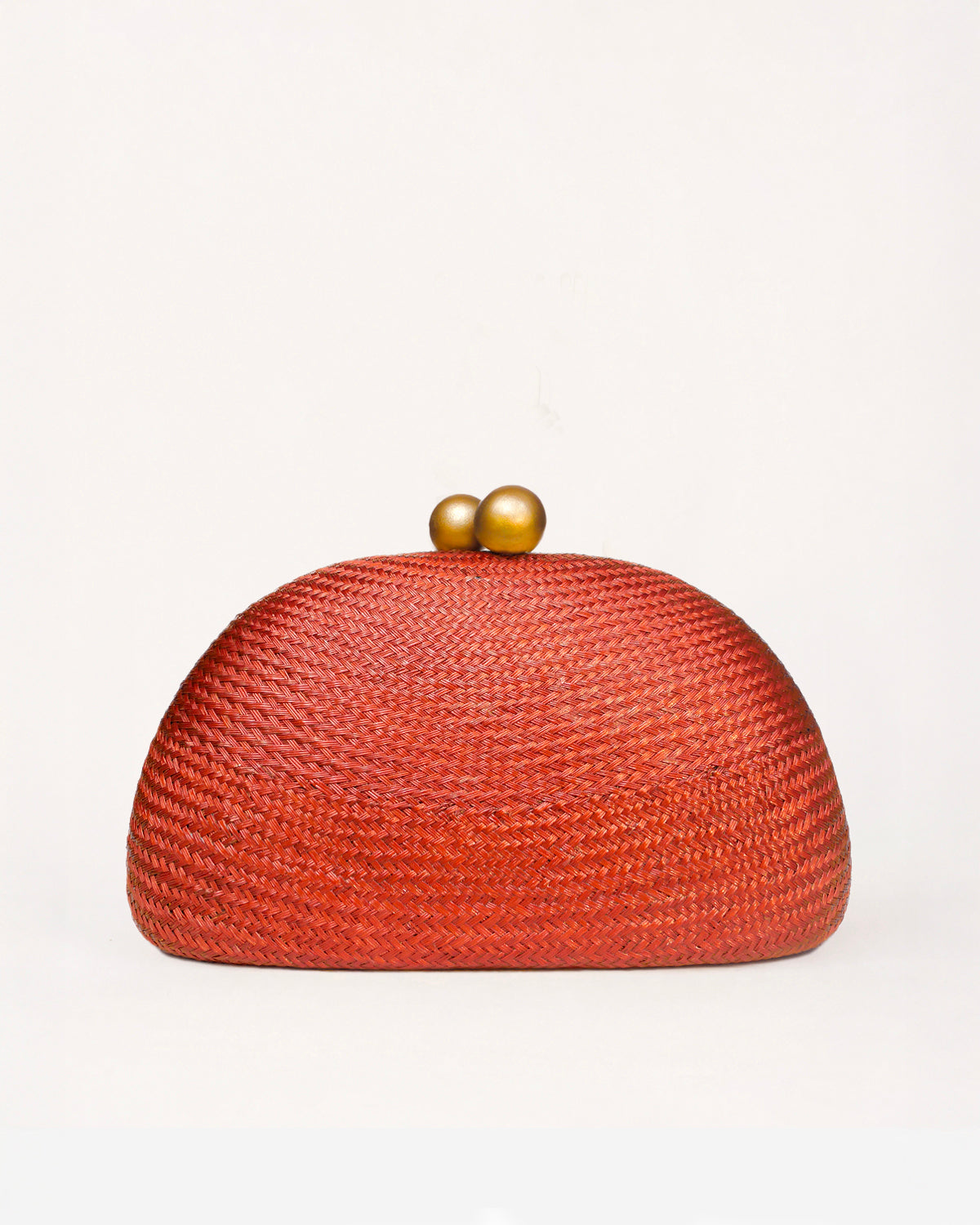 A dome-shaped woven clutch bag in a vibrant rust red-orange color, featuring a textured straw-like weave and two small metallic gold beads on top, set against a plain off-white background.