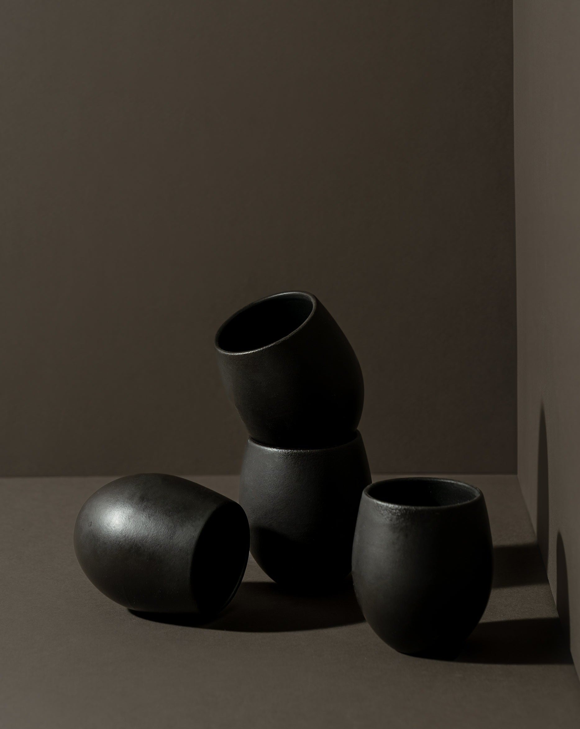 A set of four stoneware espresso tumblers in a neutral color, stacked in a pyramid shape against a neutral background.