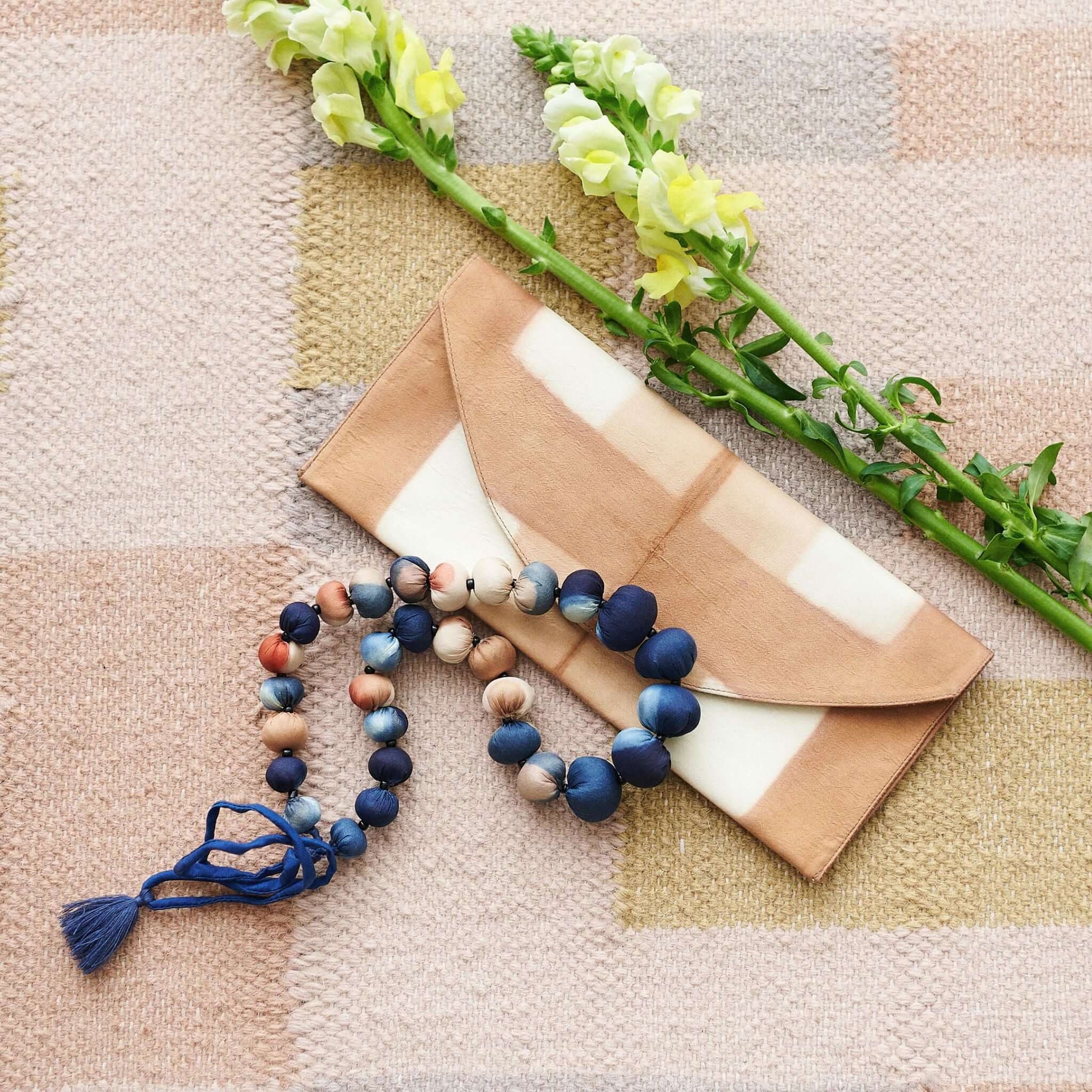Mihika silk beaded necklace displayed with a chic envelope and flowers on a textured background.